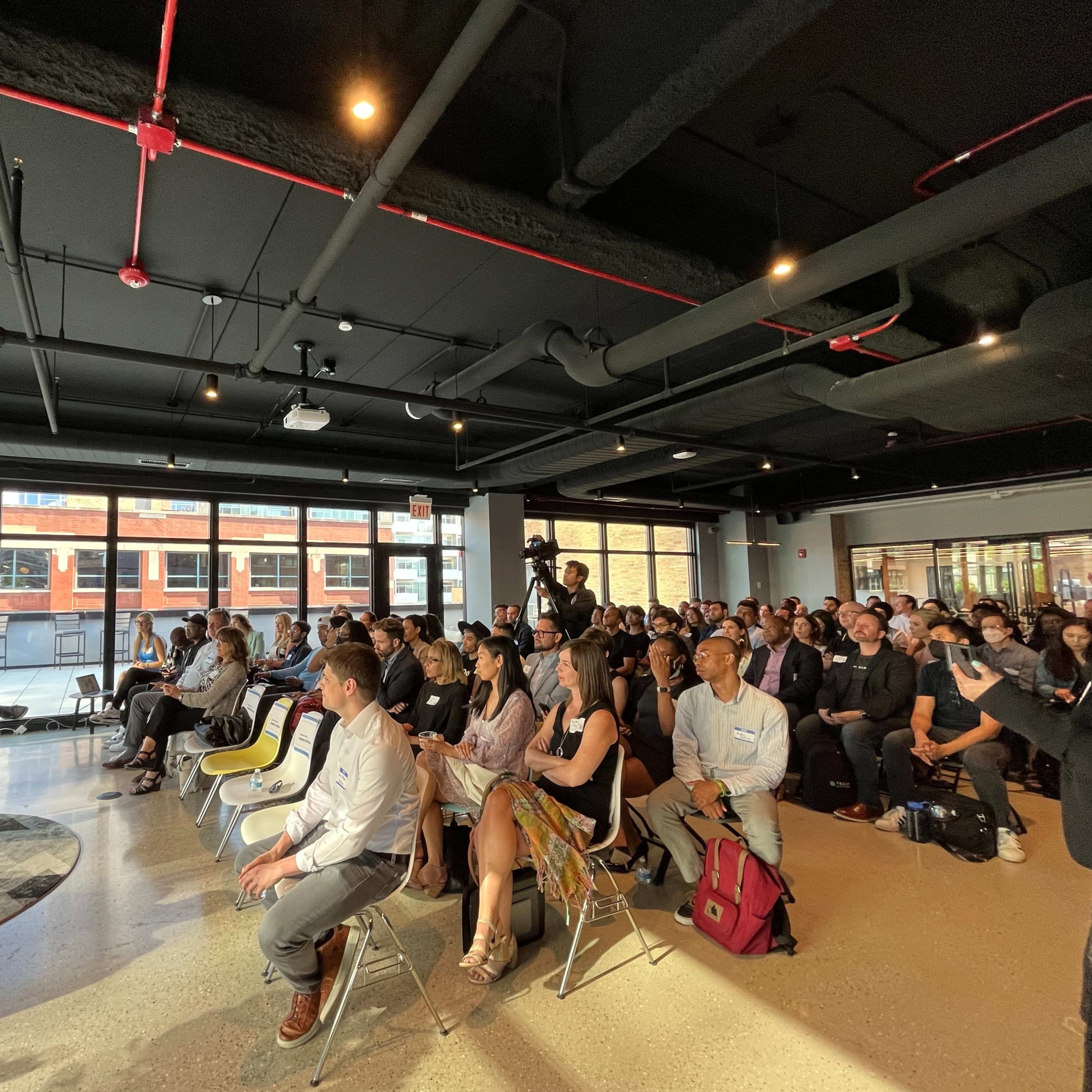 A large audience is seated in a modern conference room, attentively watching a presentation on a screen.