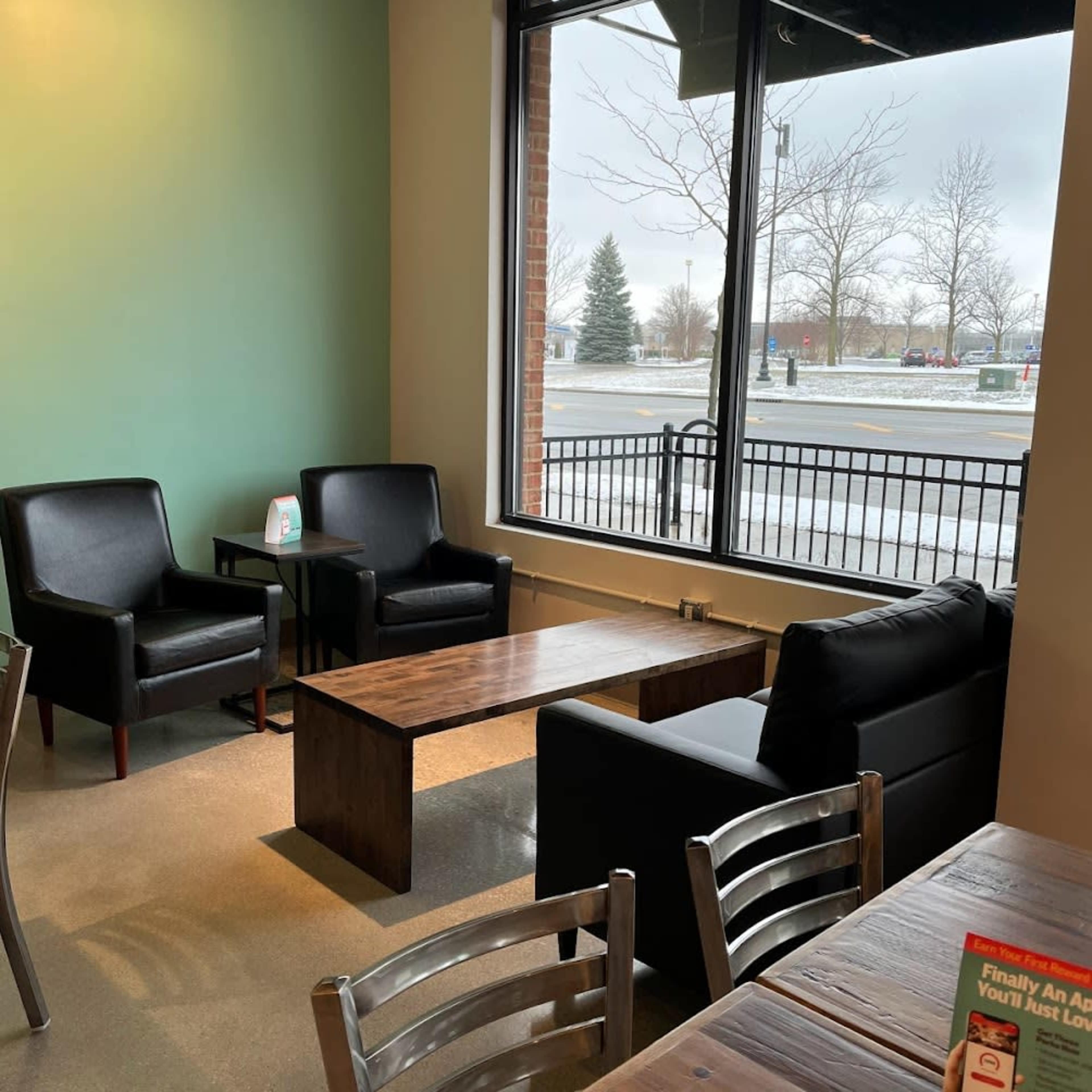 A cozy seating area in a cafe, featuring two black armchairs and a wooden coffee table under a large window.