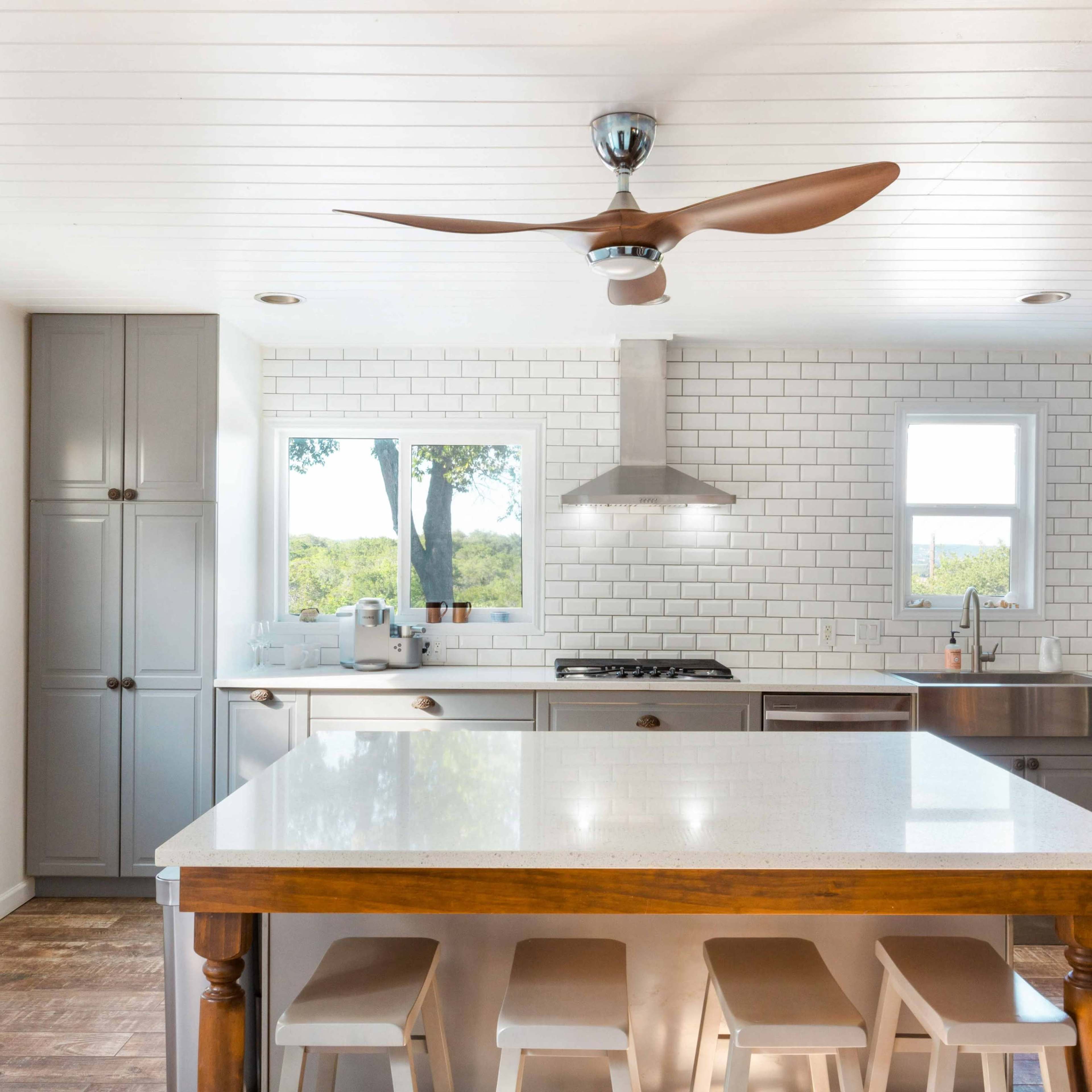 A modern kitchen features gray cabinetry, a large island with white countertops, and a stainless steel stove beneath a ceiling fan.