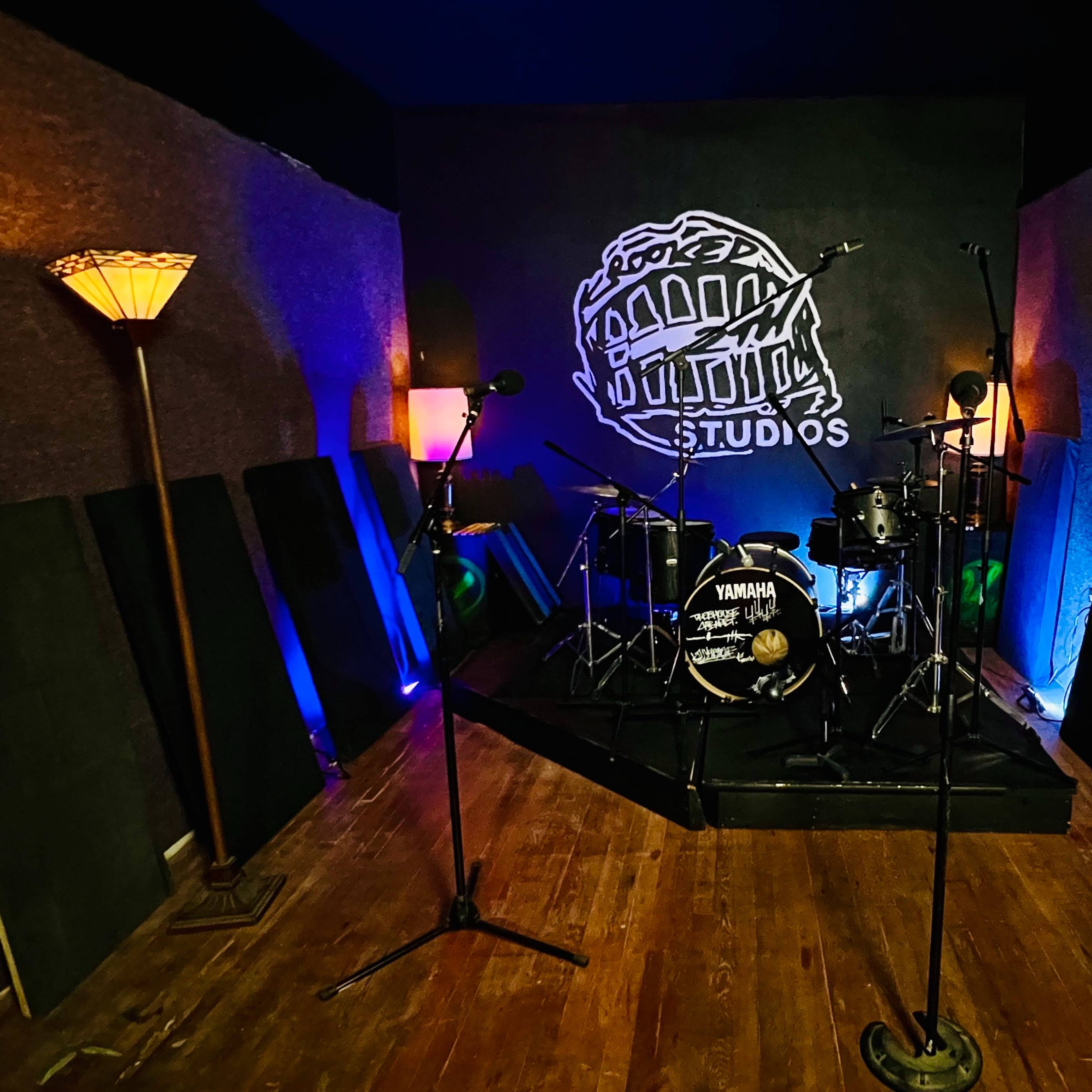 A music studio with a drum set, microphones, and ambient lighting.