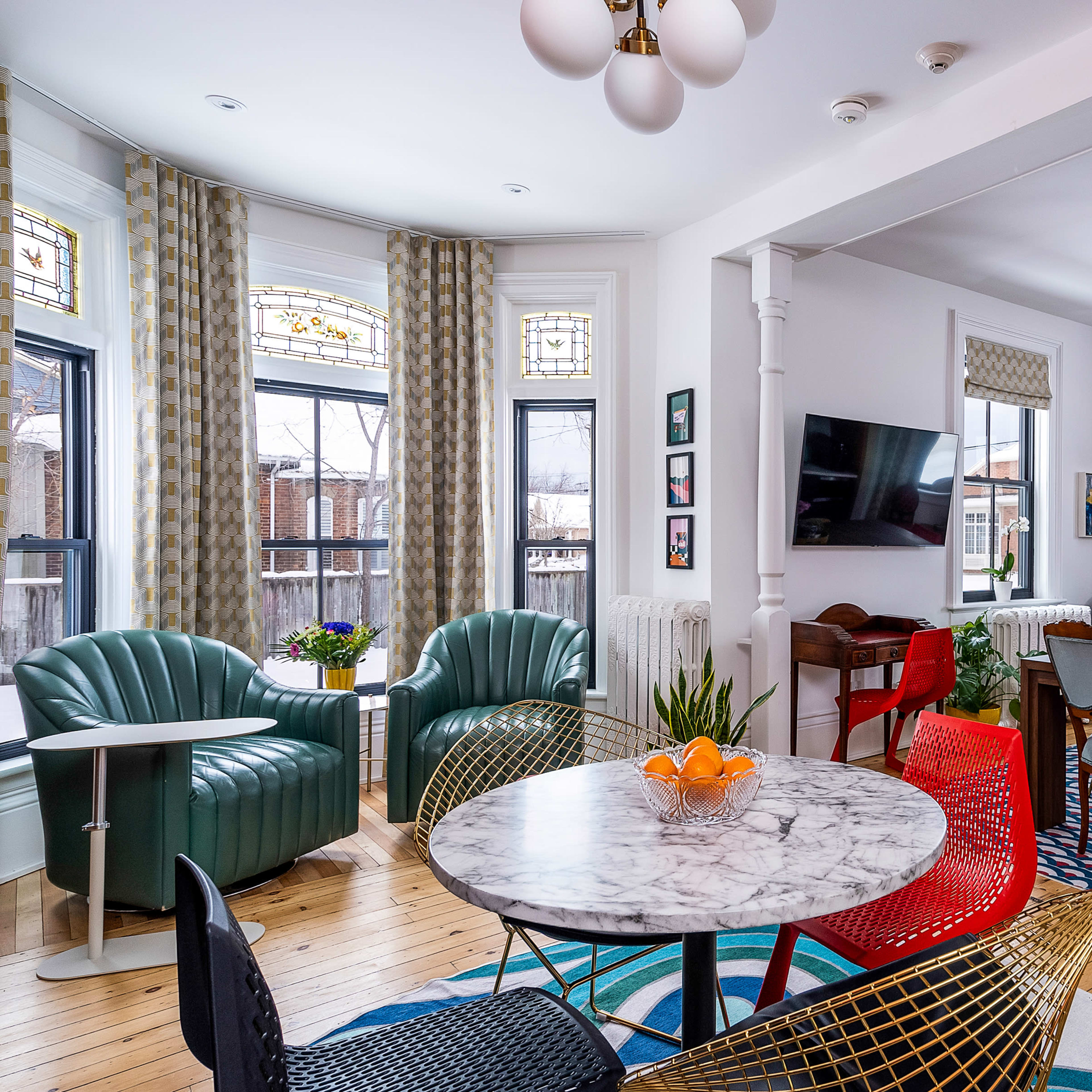 A spacious dining area featuring a round marble table, colorful chairs, and large windows with patterned curtains.