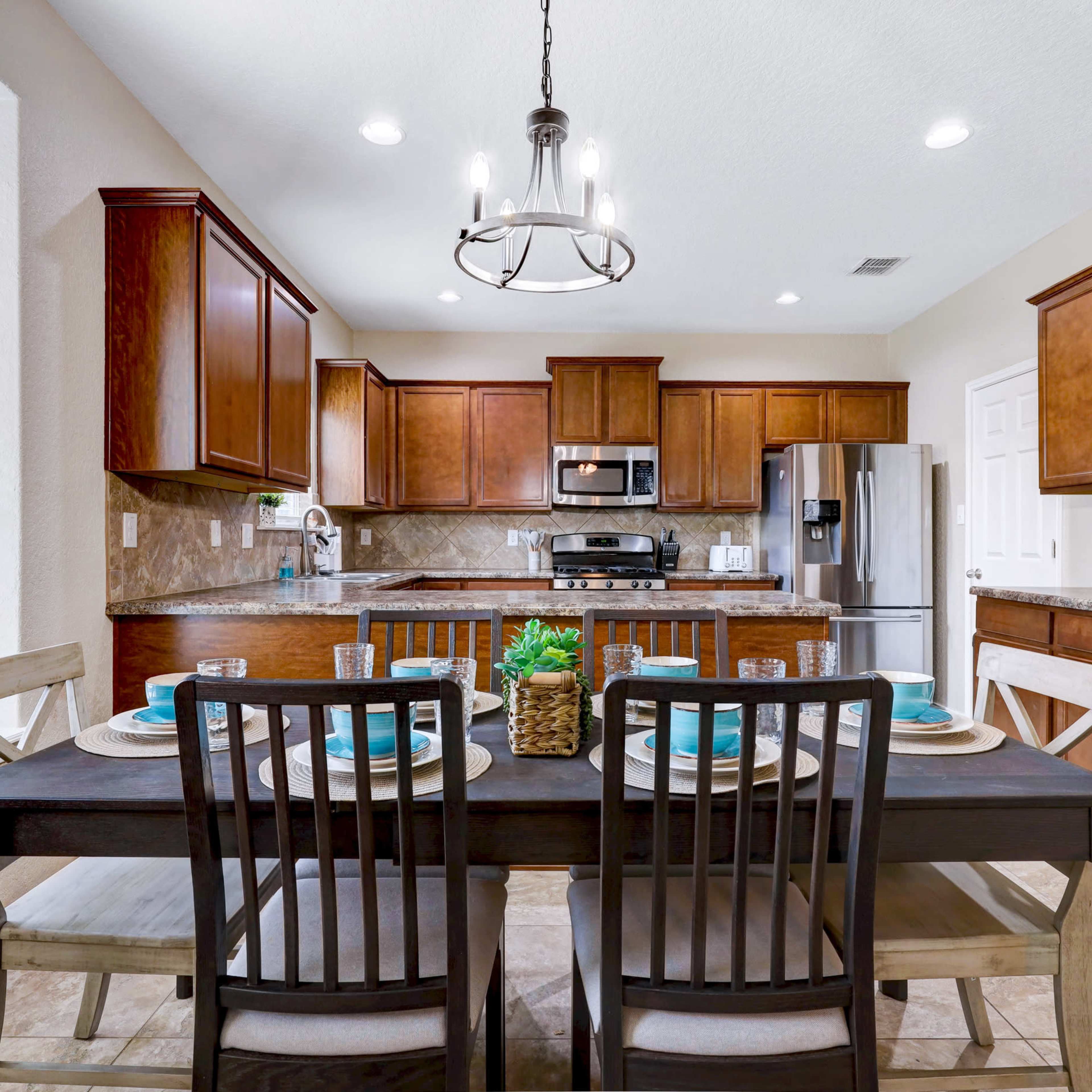 A modern kitchen with dark wooden cabinets and stainless steel appliances features a dining table set for four.