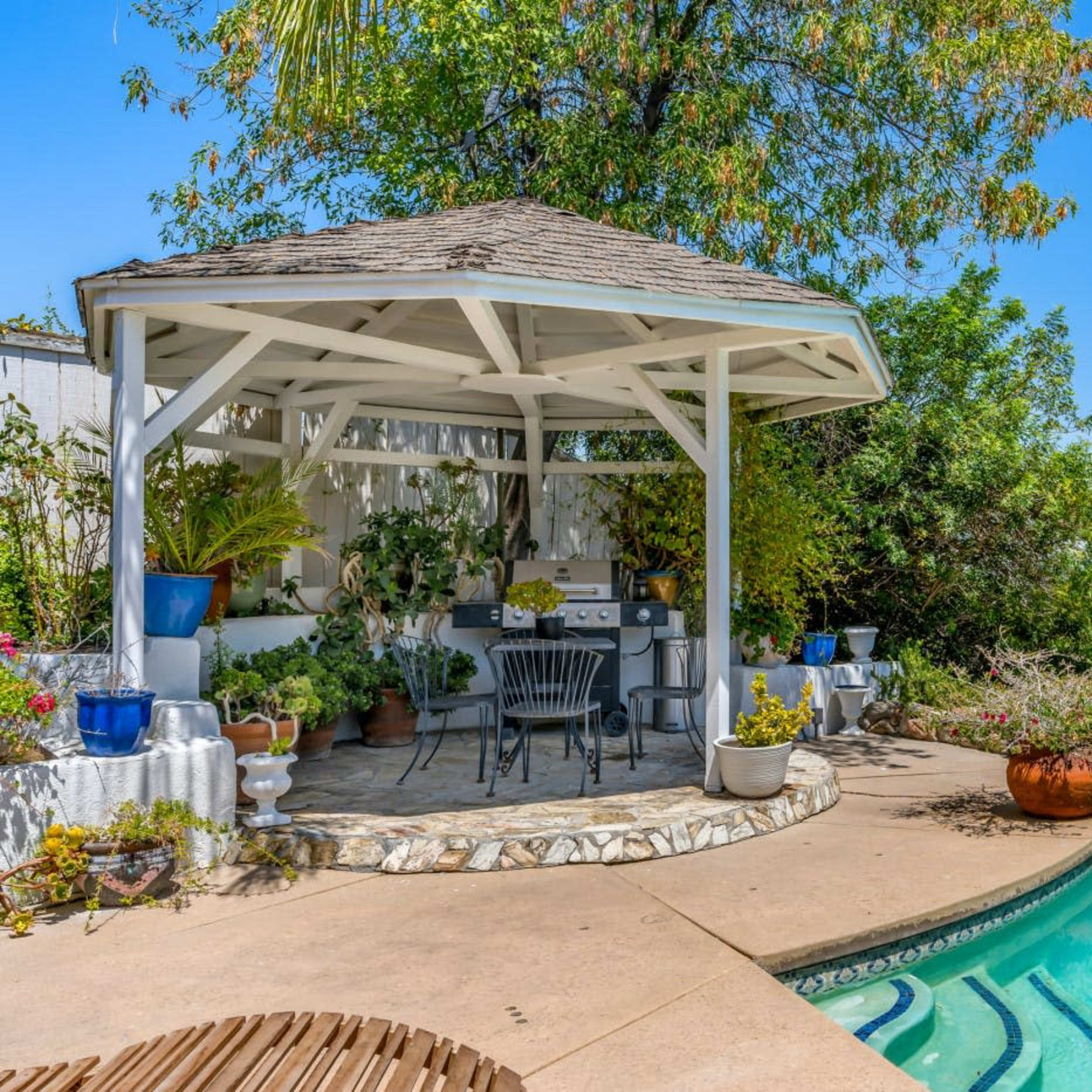 A gazebo with seating overlooks a swimming pool, surrounded by landscaped greenery and distant city views.
