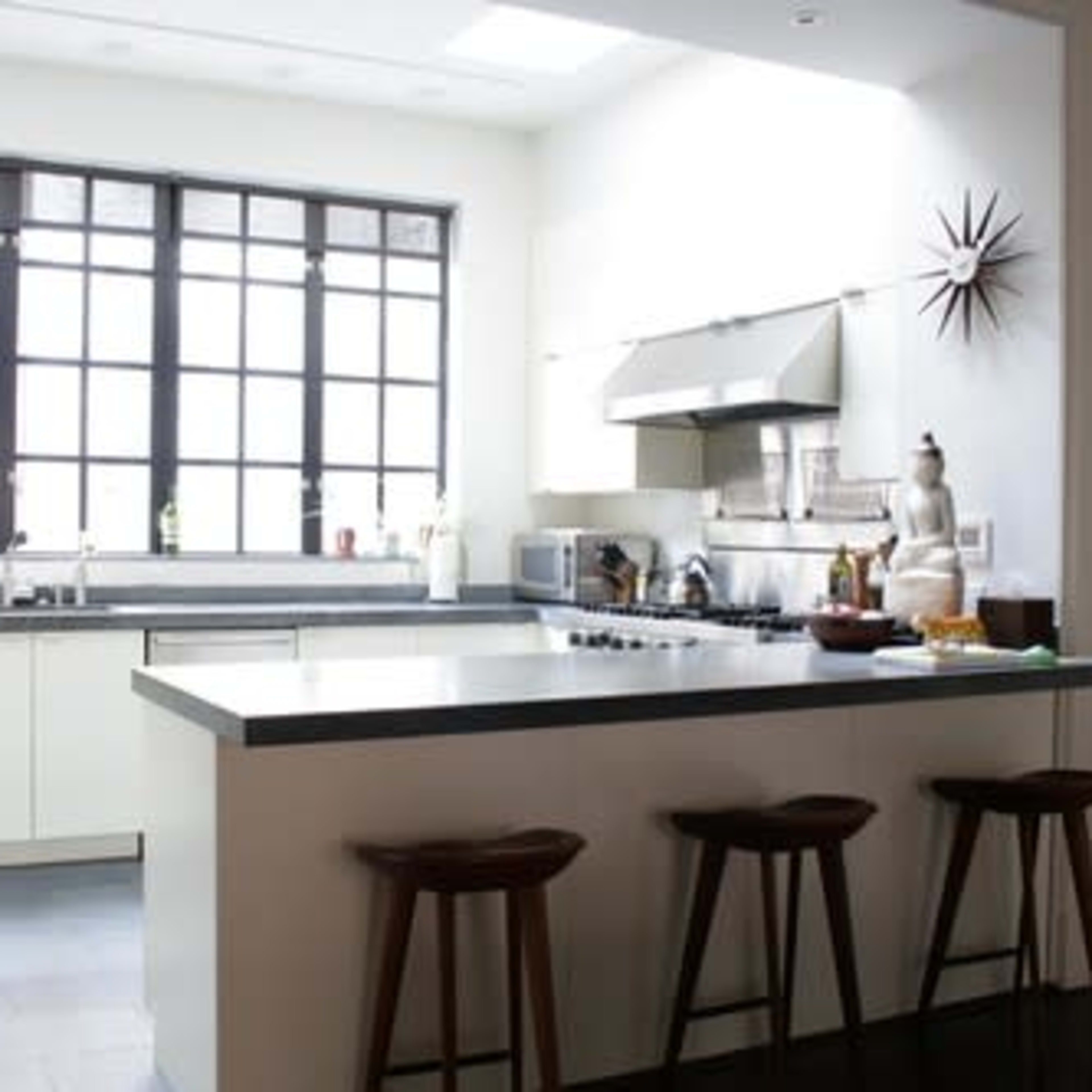 A modern kitchen with a central island, stainless steel appliances, and large windows allowing natural light.