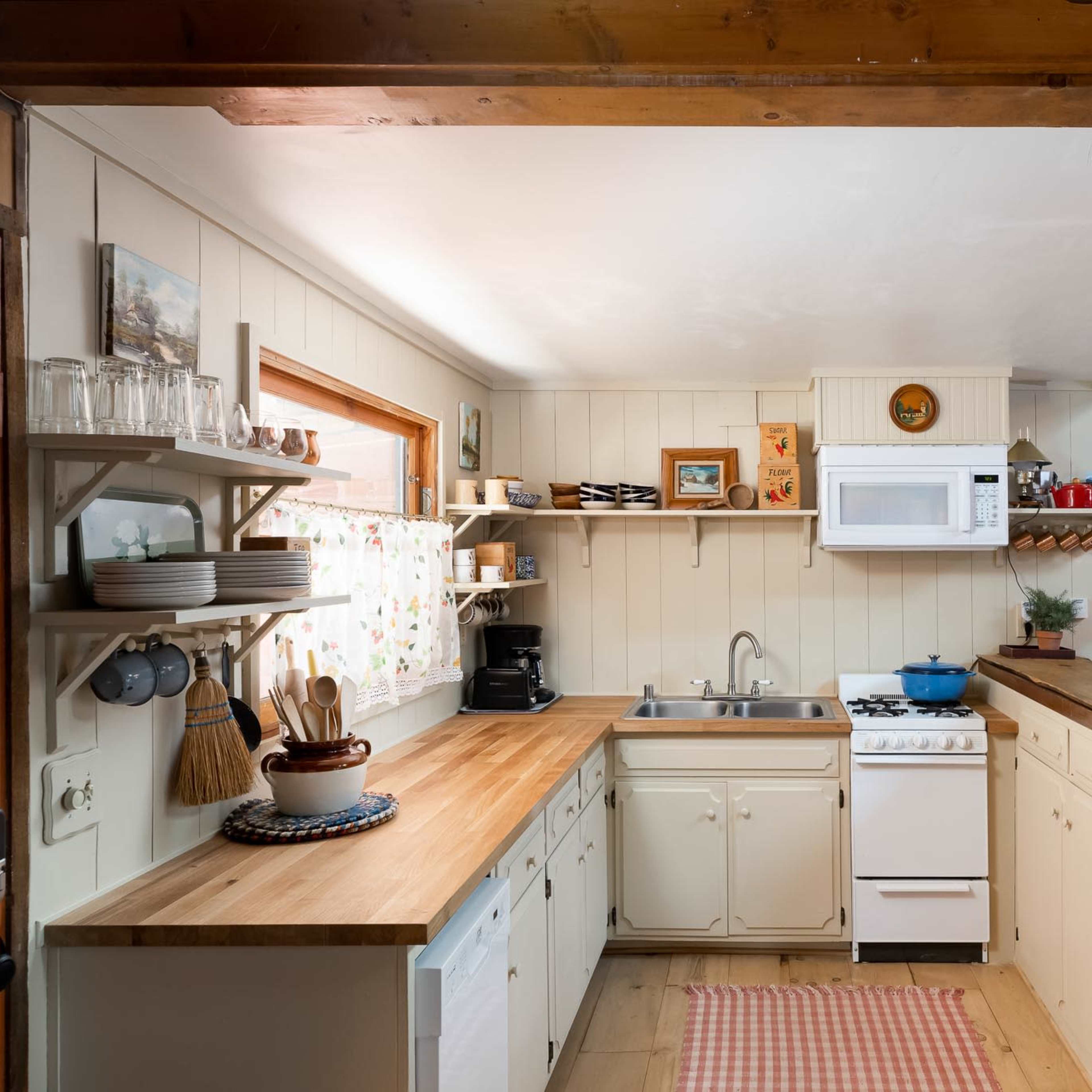 A compact kitchen with wooden countertops, a sink, a stove, and a microwave, featuring light-colored walls and wooden accents.