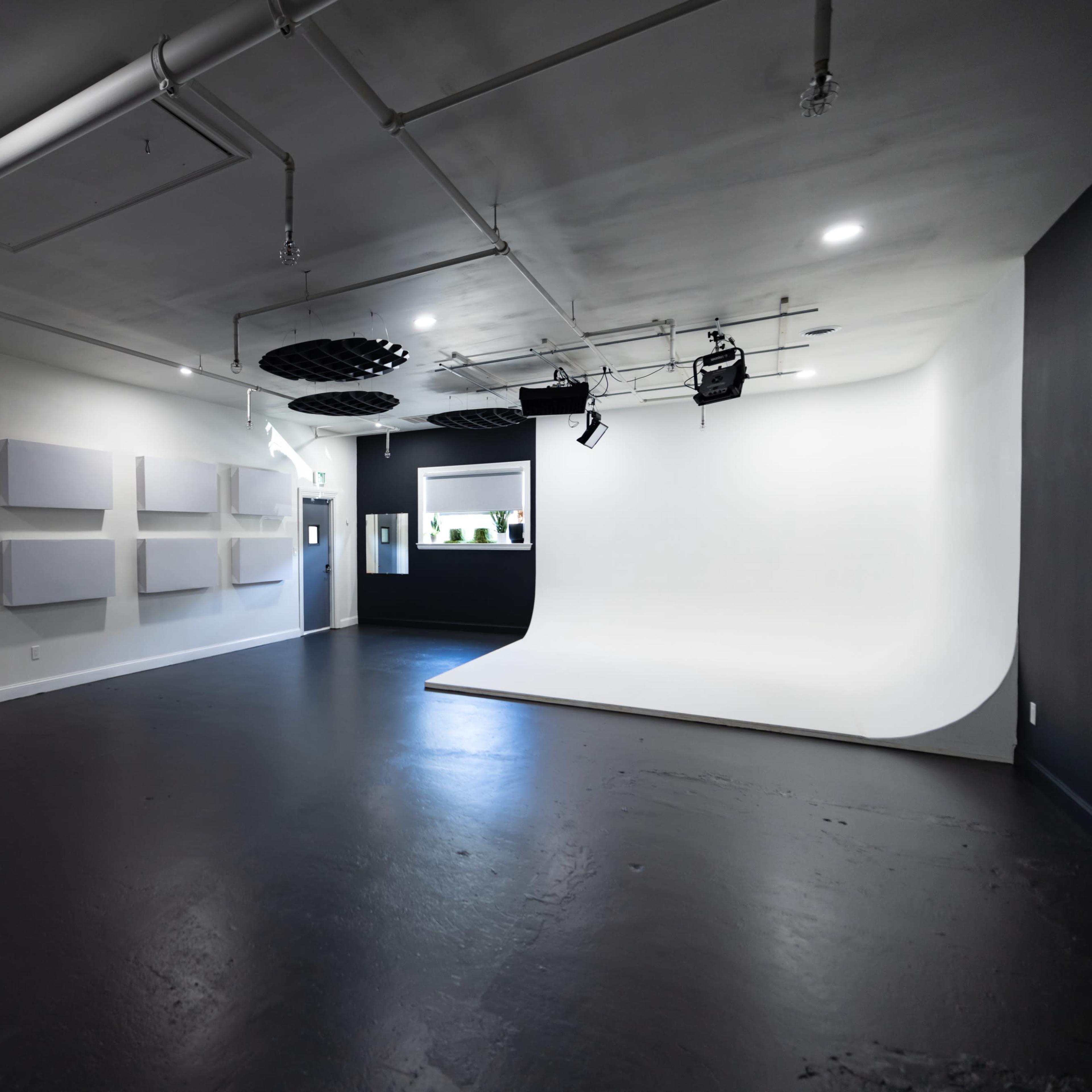 A spacious, empty studio with gray soundproof panels on the walls and a white cyclorama backdrop in one corner.