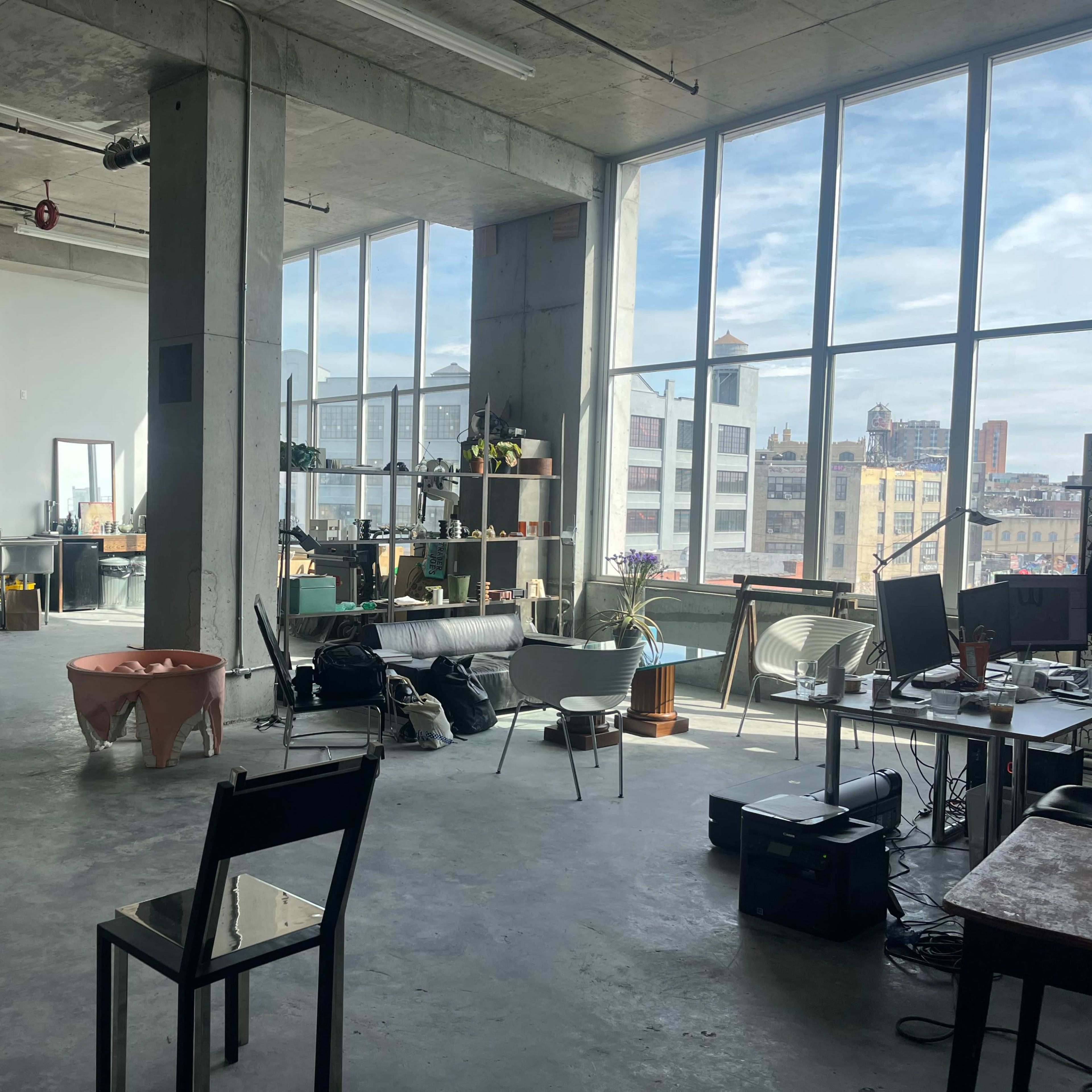 An industrial-style loft with large windows, concrete floors, and various furniture and equipment scattered throughout the space.