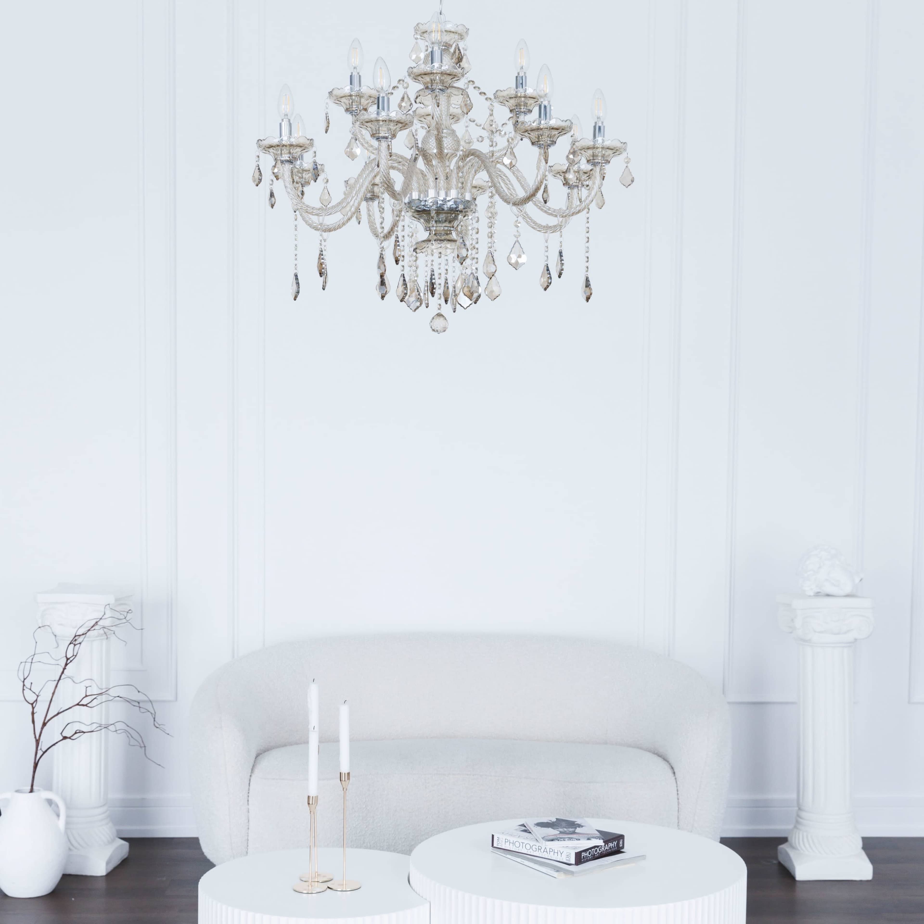 A minimalist room featuring a light-colored sofa, a circular coffee table with a book and candles, and an ornate chandelier hanging from the ceiling.