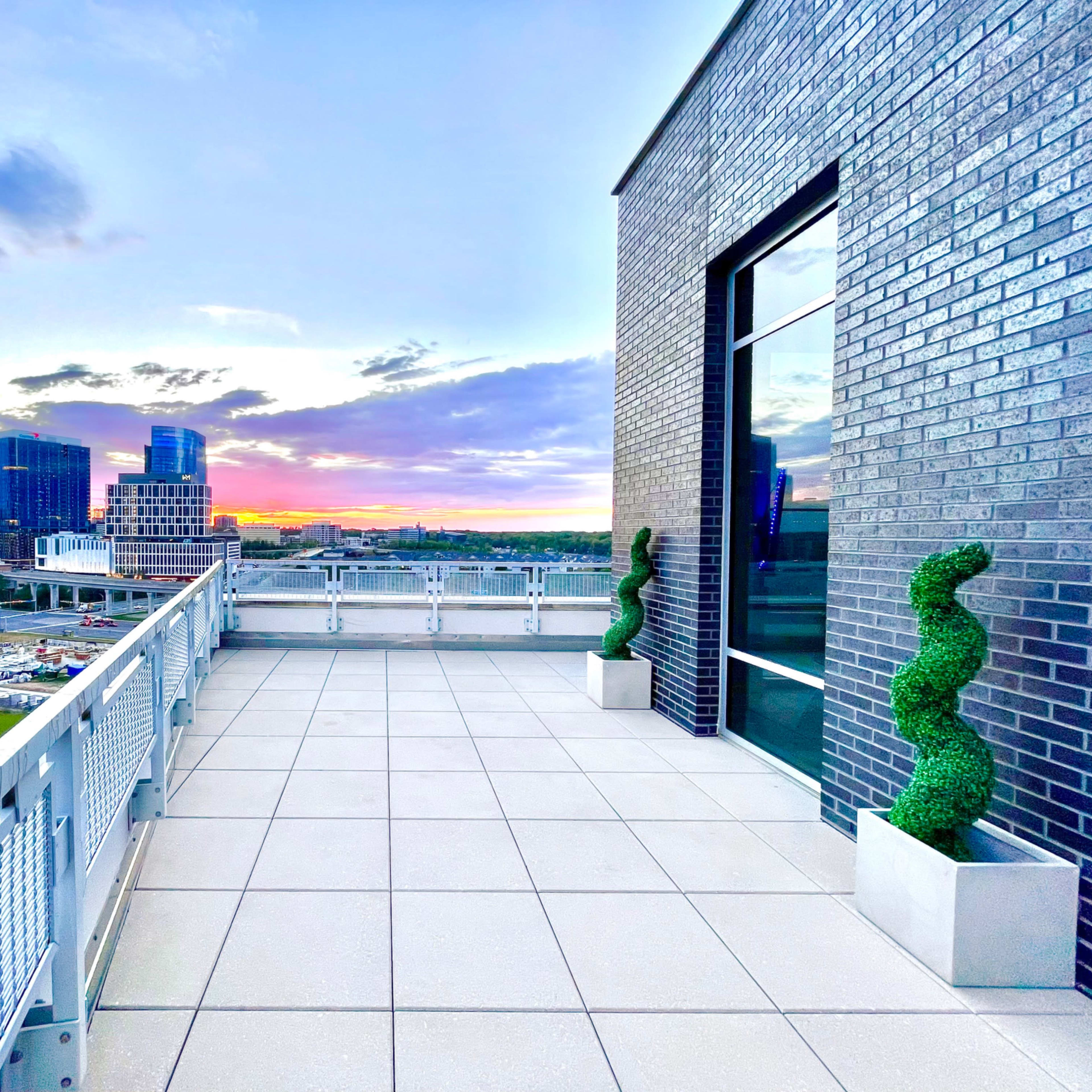 A modern balcony with decorative topiary and a view of a city skyline at sunset.