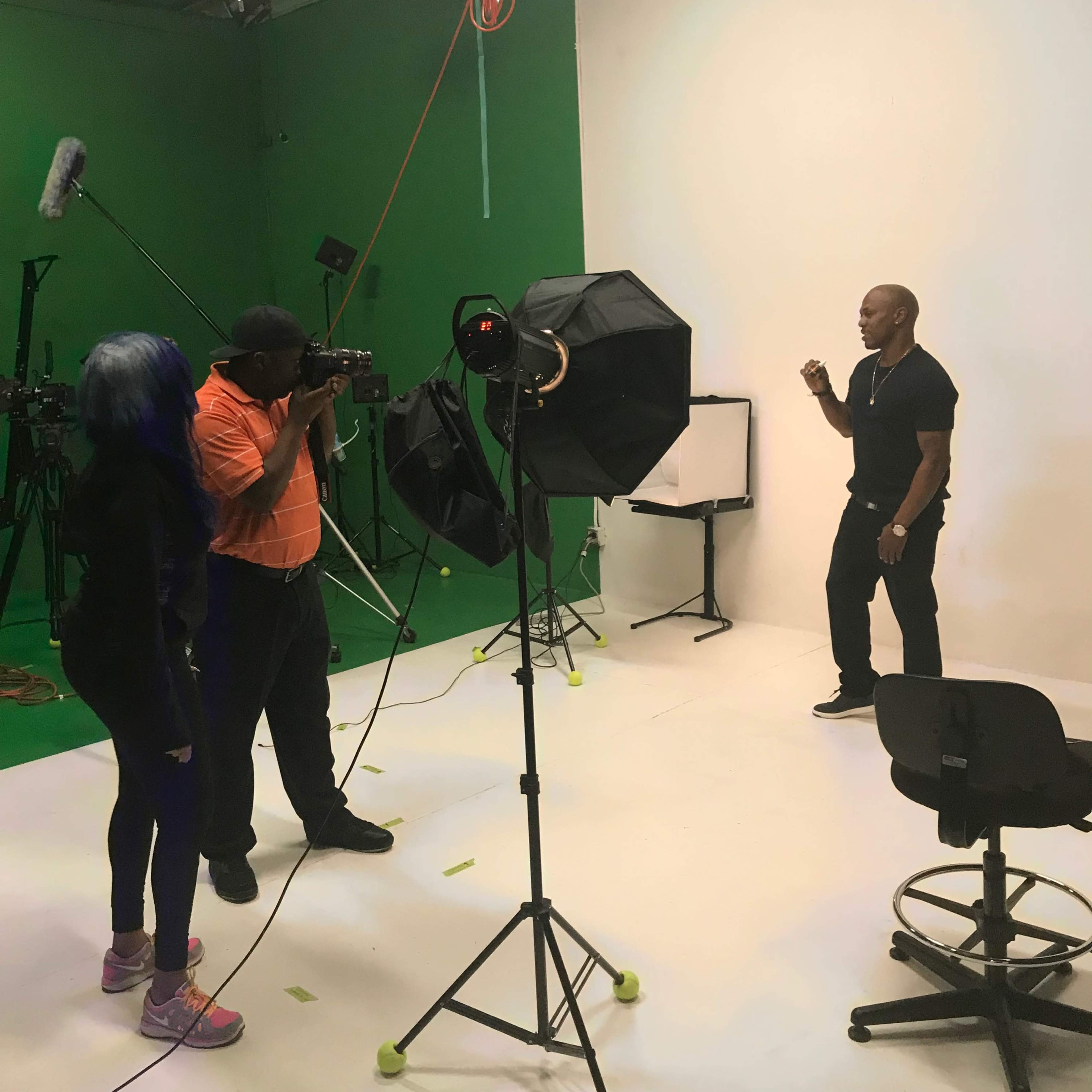 A photographer captures a man posing in a studio with a green screen and various filming equipment.