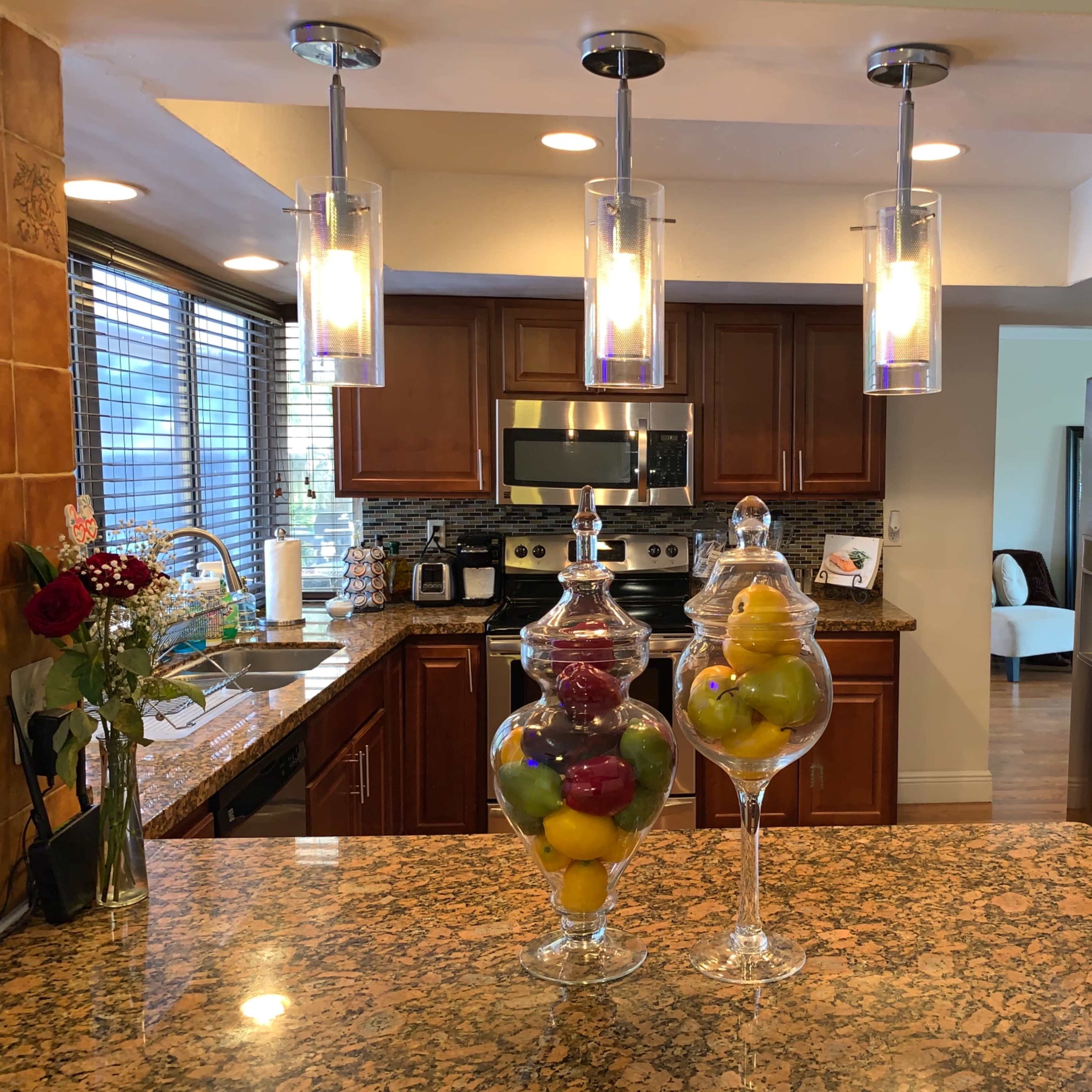 A modern kitchen with wooden cabinets, a granite countertop, and decorative glass jars filled with colorful fruits.