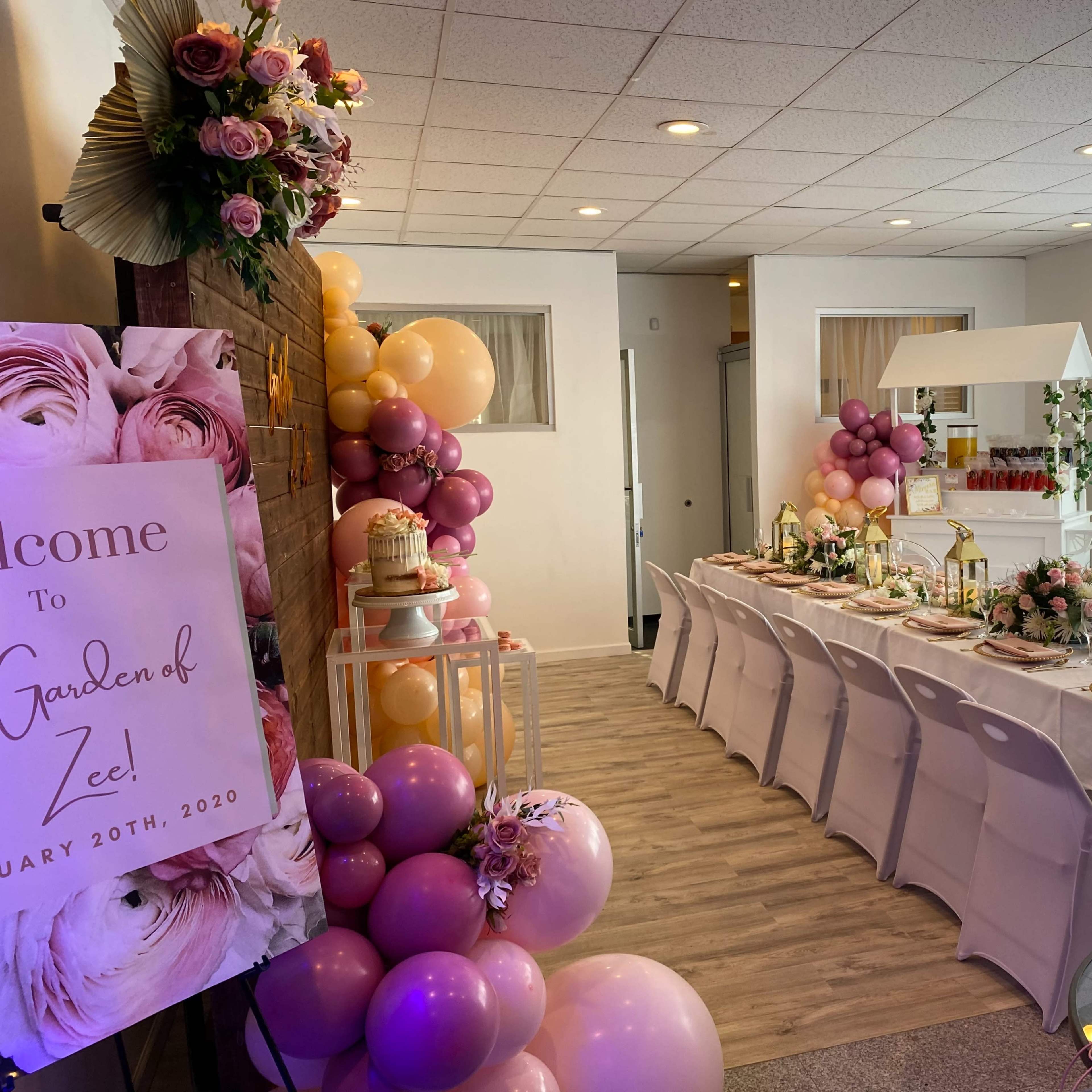 A decorated banquet room with a long table set for a celebration, surrounded by floral arrangements and balloons.