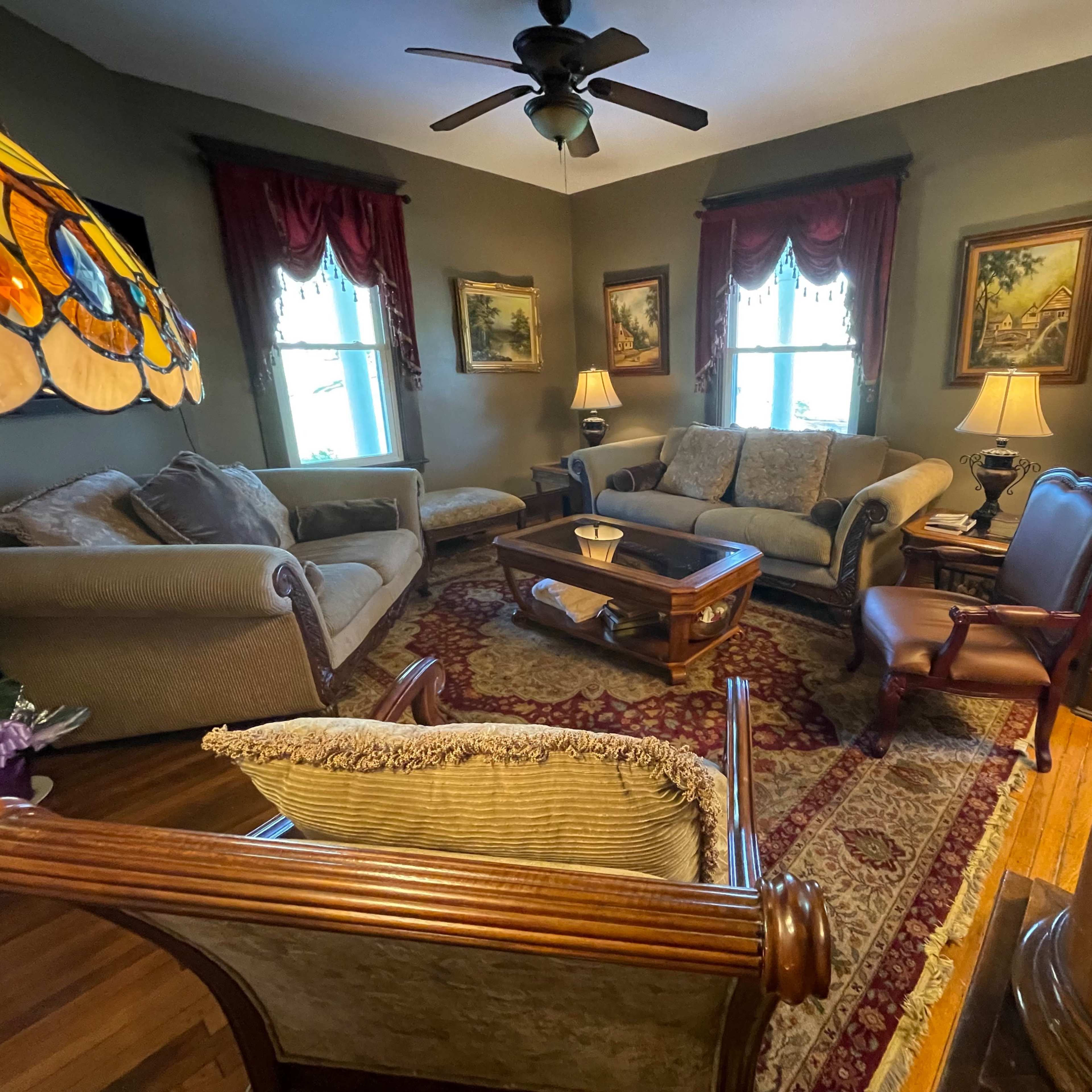 A cozy living room with a couch, armchairs, and a wooden coffee table, adorned with framed artwork and a stained glass lamp.