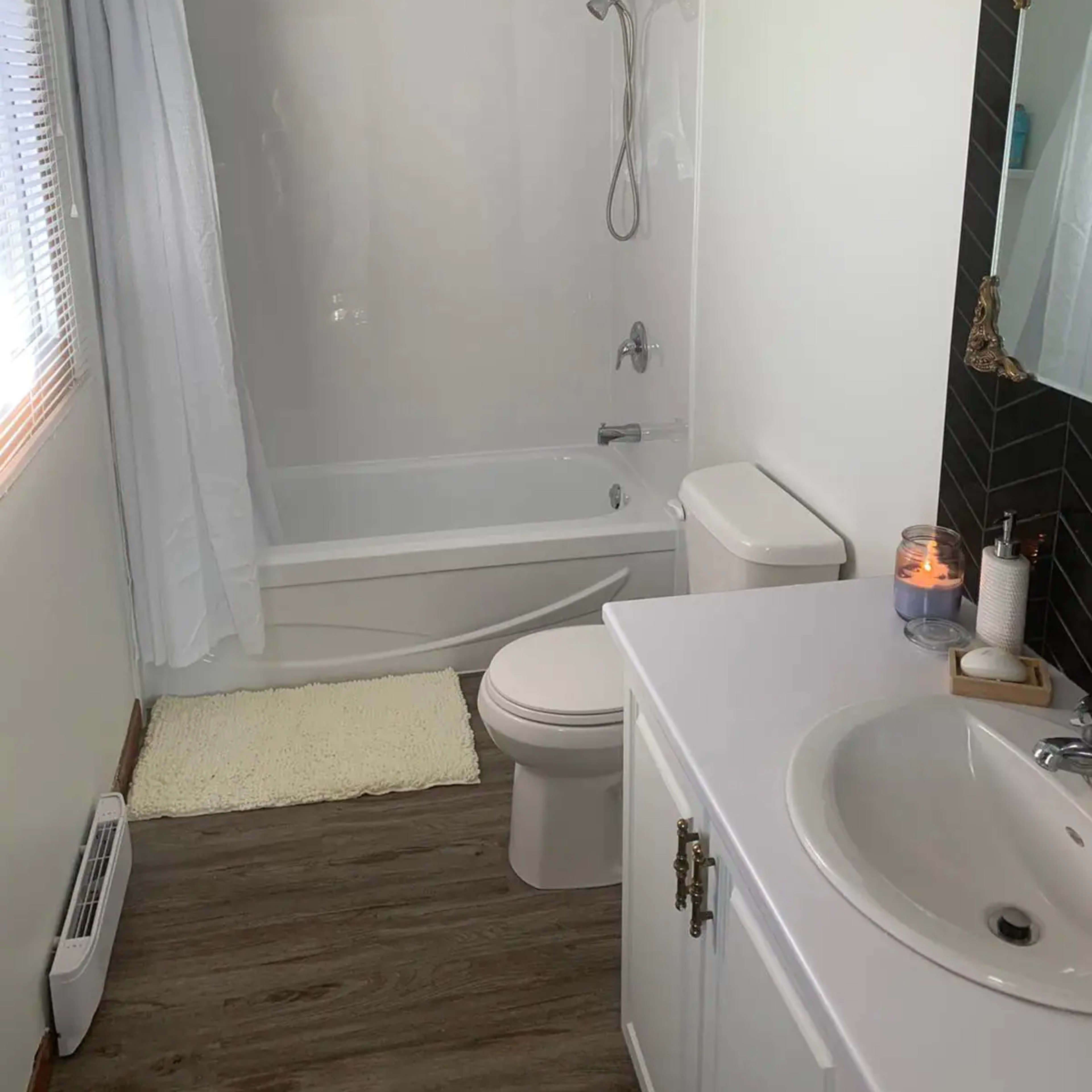 A clean, modern bathroom featuring a bathtub with a showerhead, a toilet, and a sink with a mirror.
