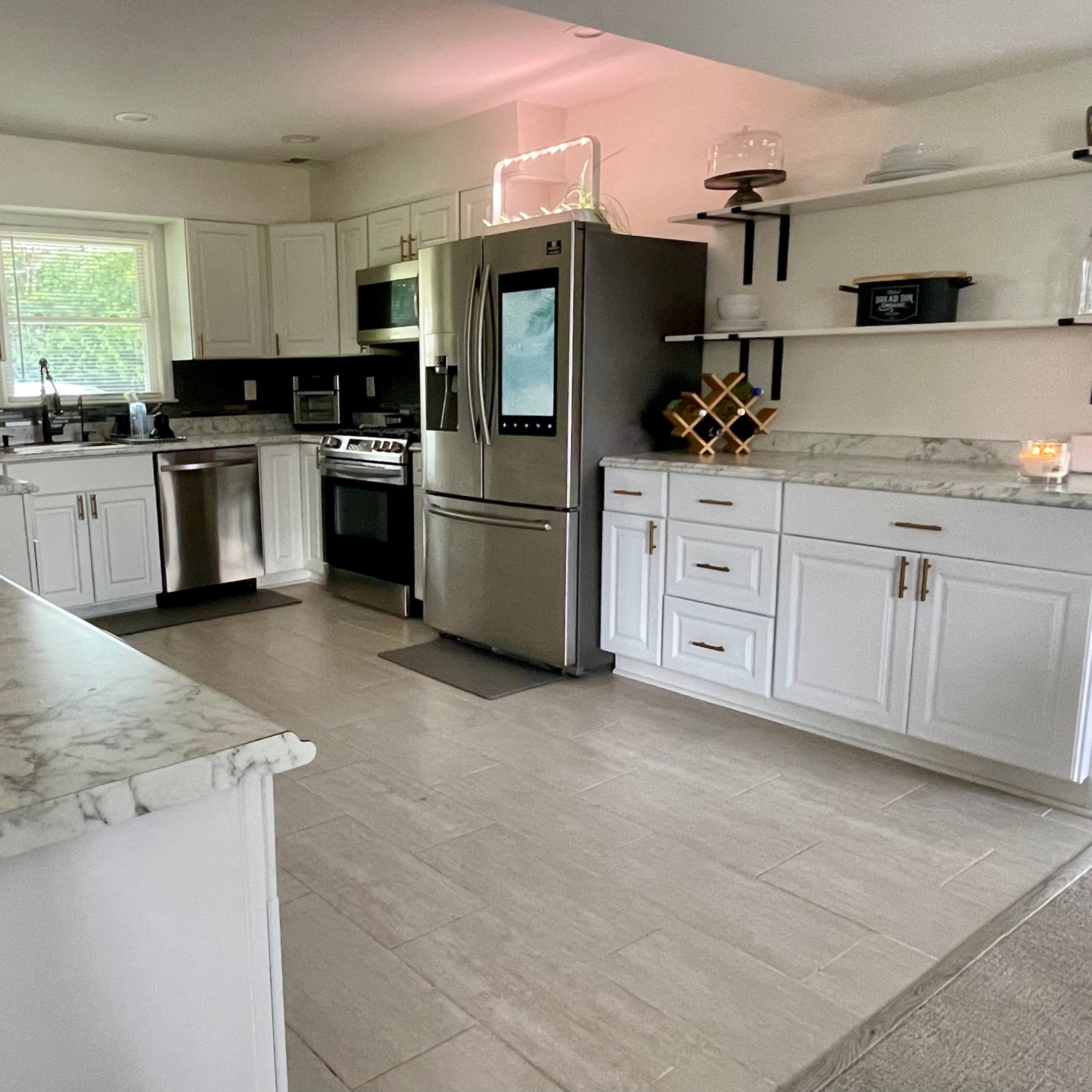 The kitchen features white cabinets, stainless steel appliances, and a marble countertop with open shelving.