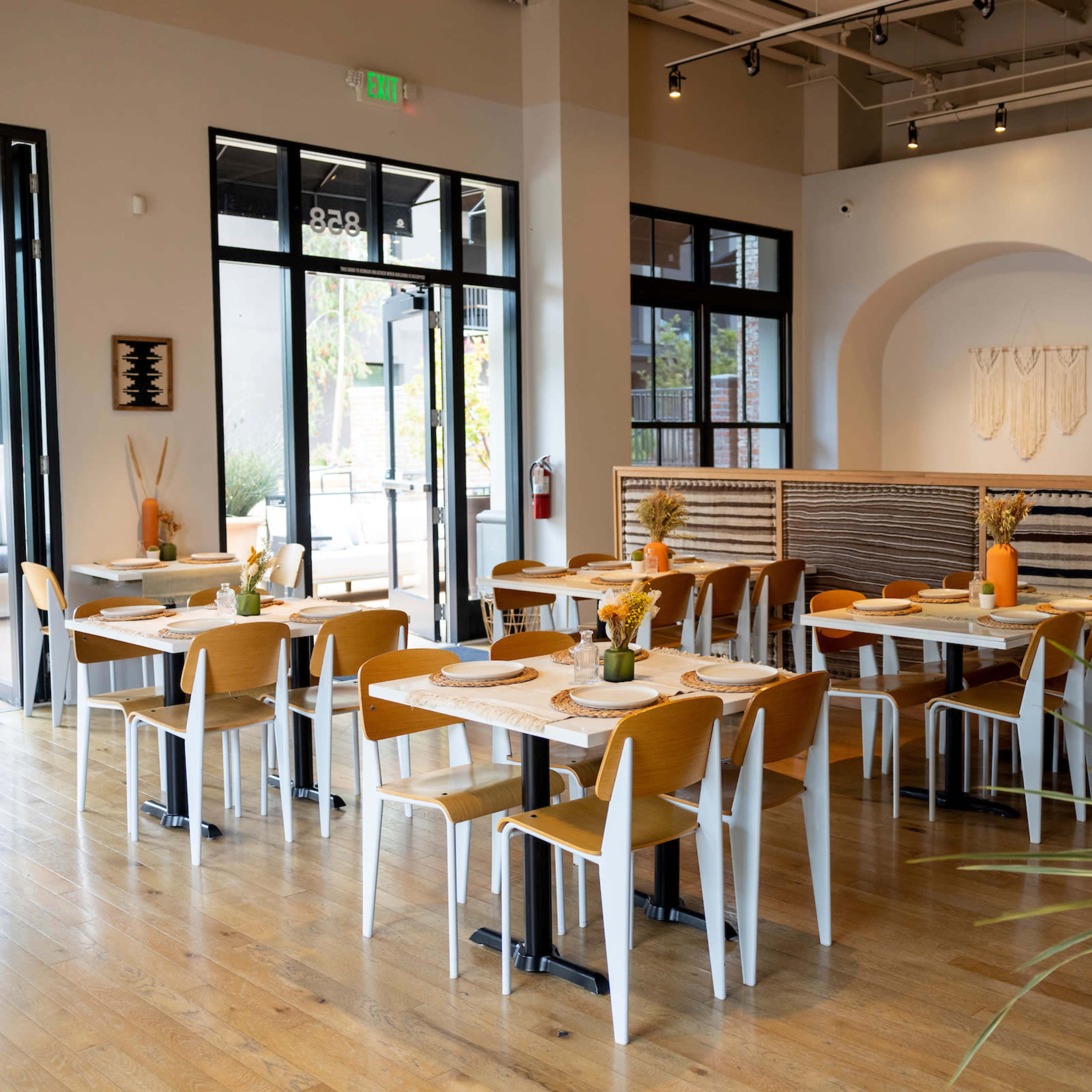A modern restaurant interior with wooden tables and chairs, large windows, and decorative wall art.