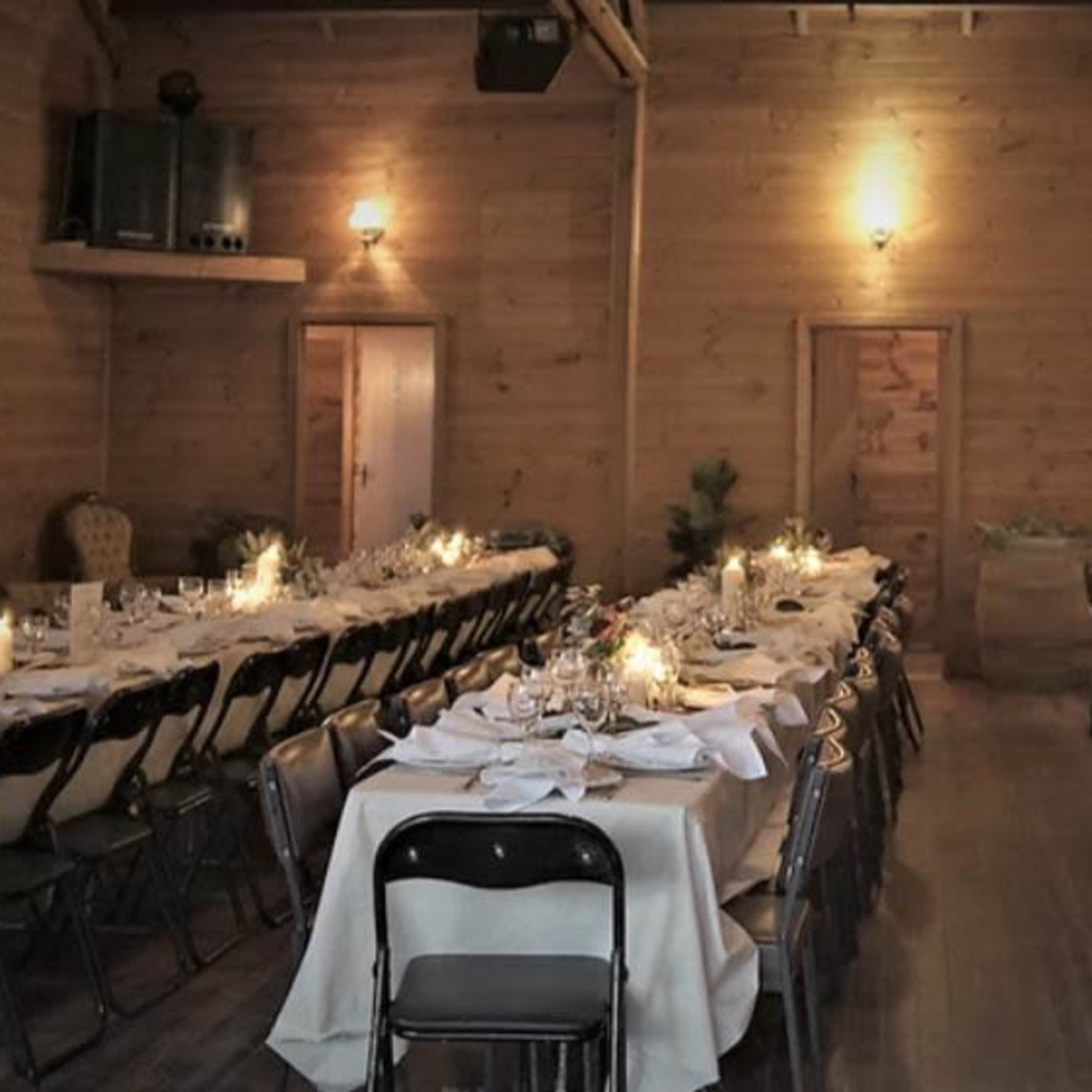 A long hall features neatly arranged tables set for a formal dinner, with candlelight illuminating the wooden interior.