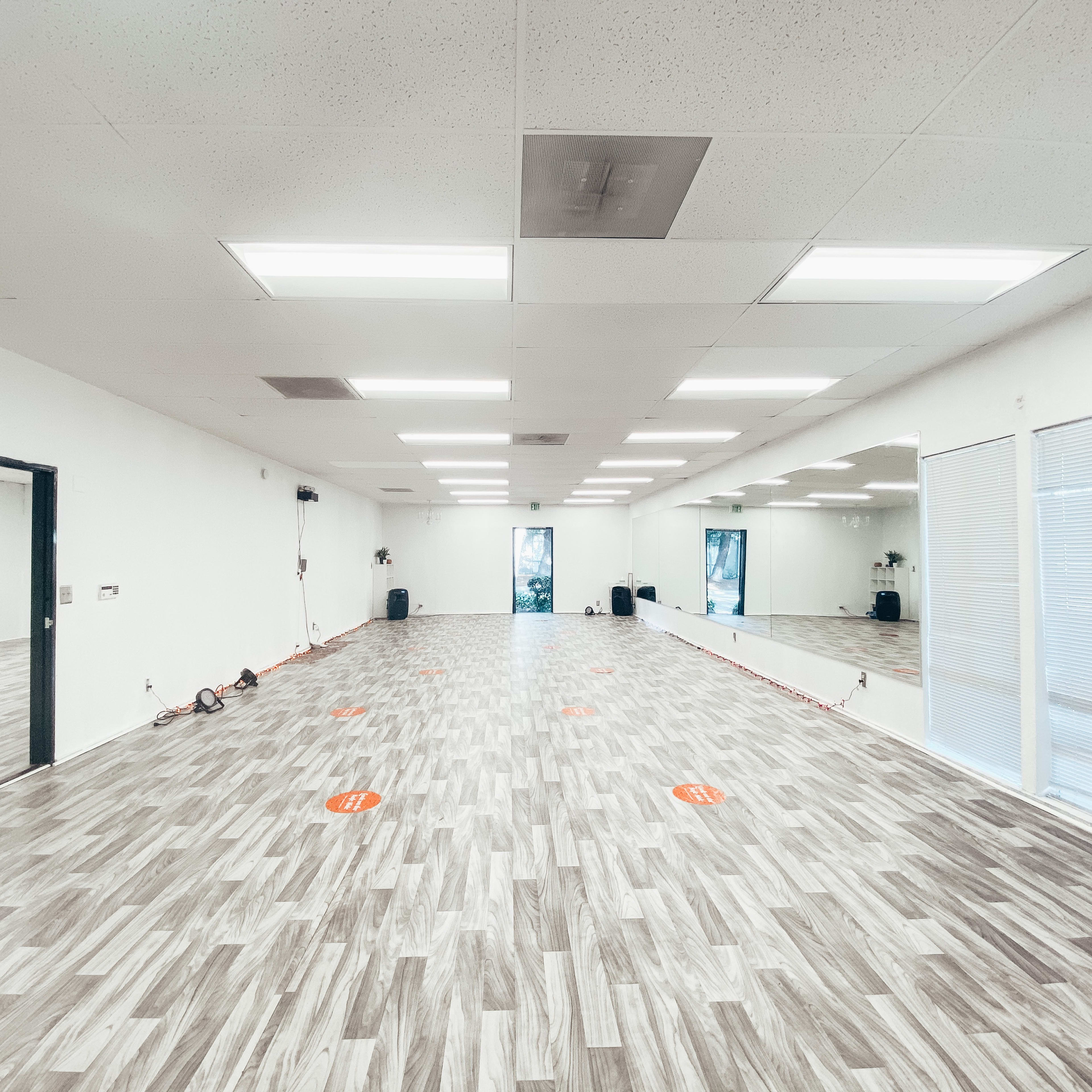 An empty, well-lit studio space with a hardwood floor and several large mirrors along the walls.