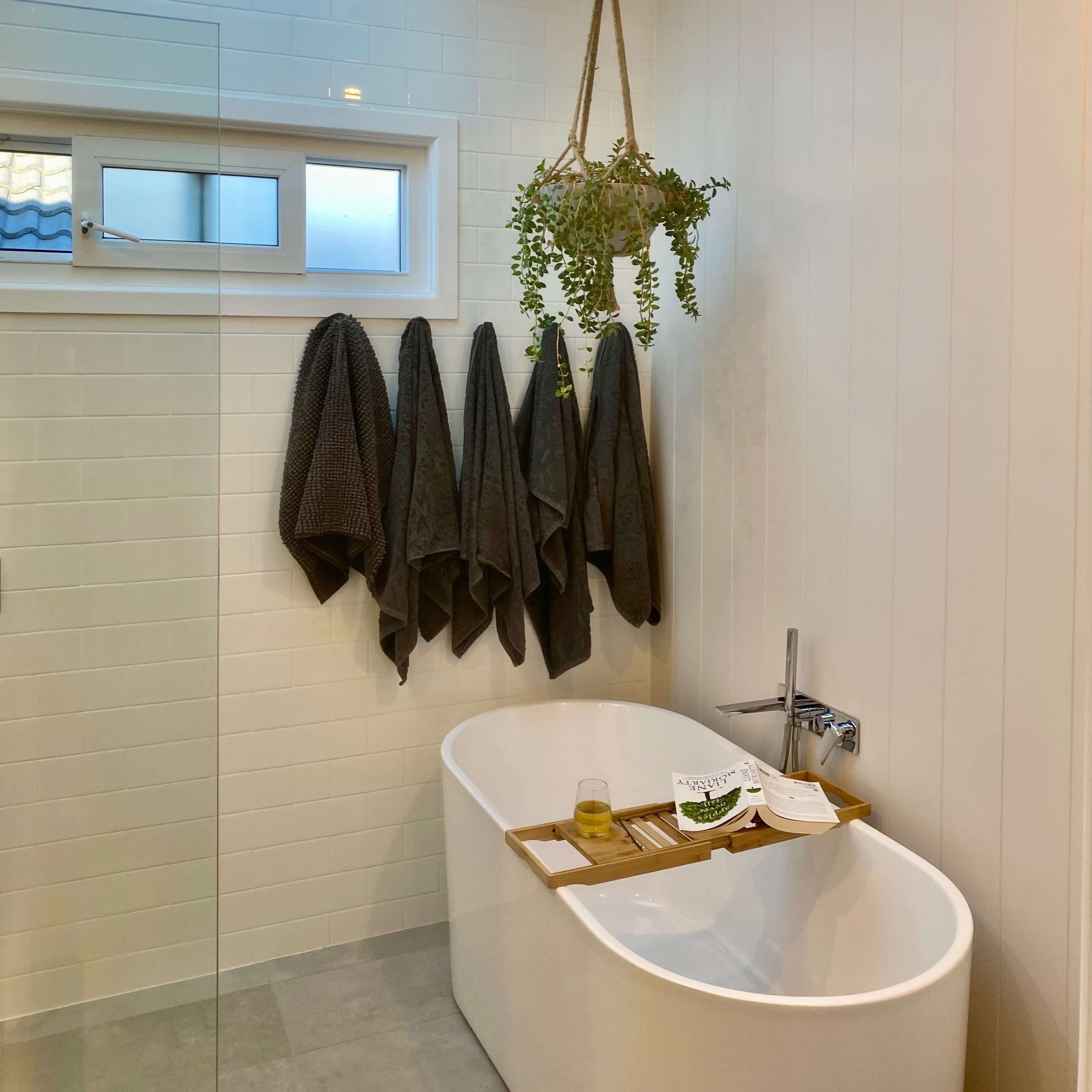 The bathroom features a freestanding bathtub beneath a skylight, with a hanging plant and neatly arranged towels on the wall.