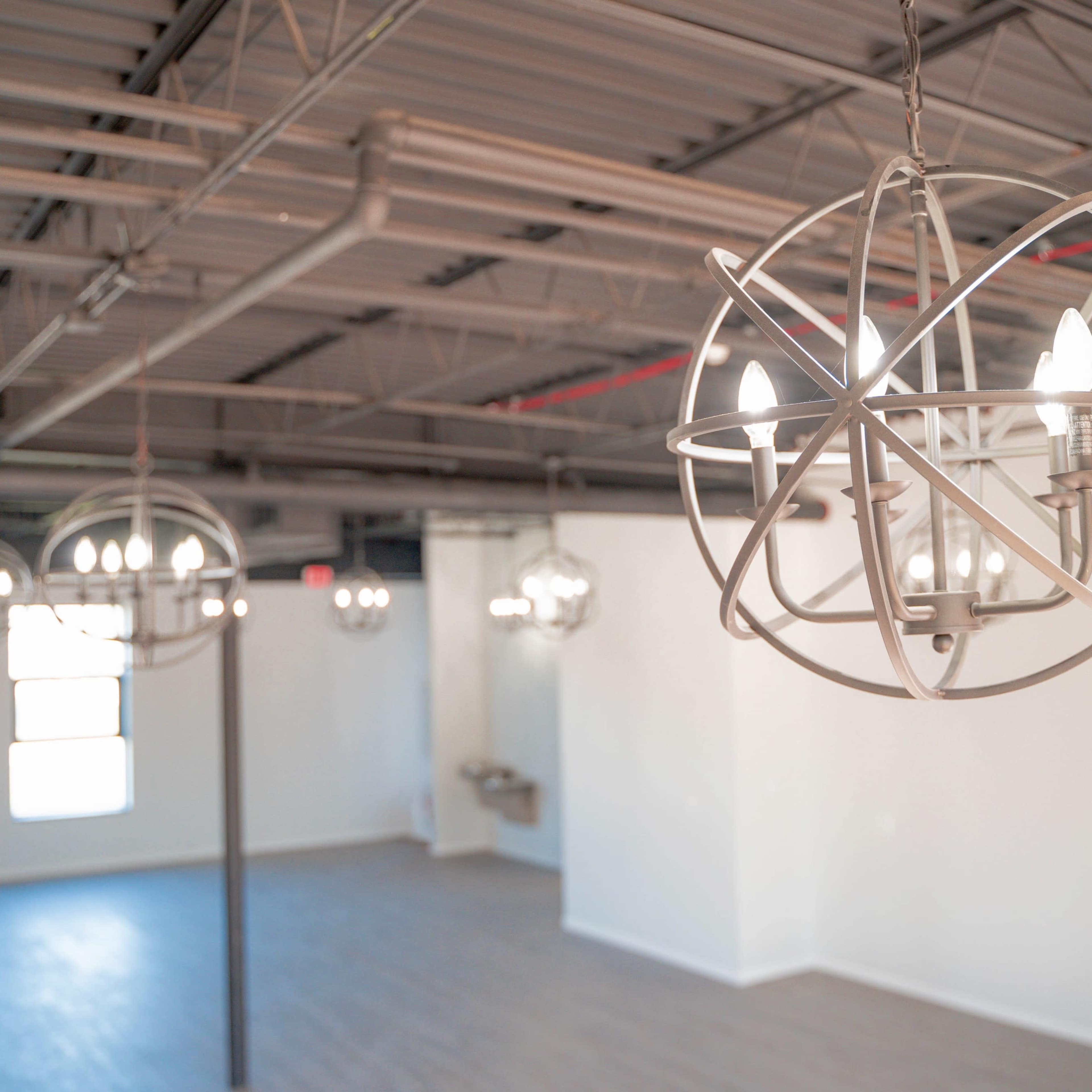 A spacious room with modern pendant chandeliers hanging from the ceiling and large windows allowing natural light to enter.