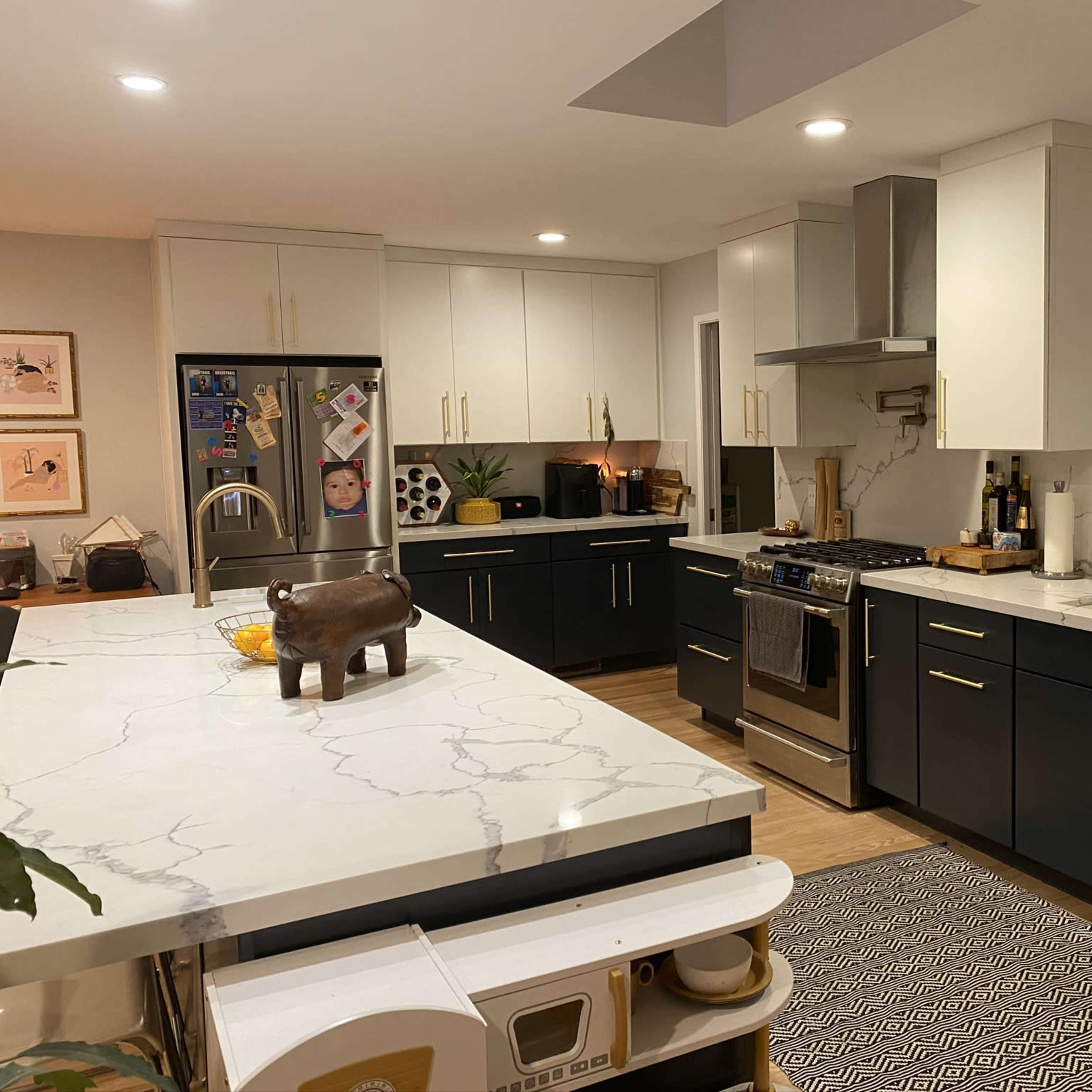 A modern kitchen featuring dark cabinets, light countertops with veining, stainless steel appliances, and a central island with a decorative item on it.
