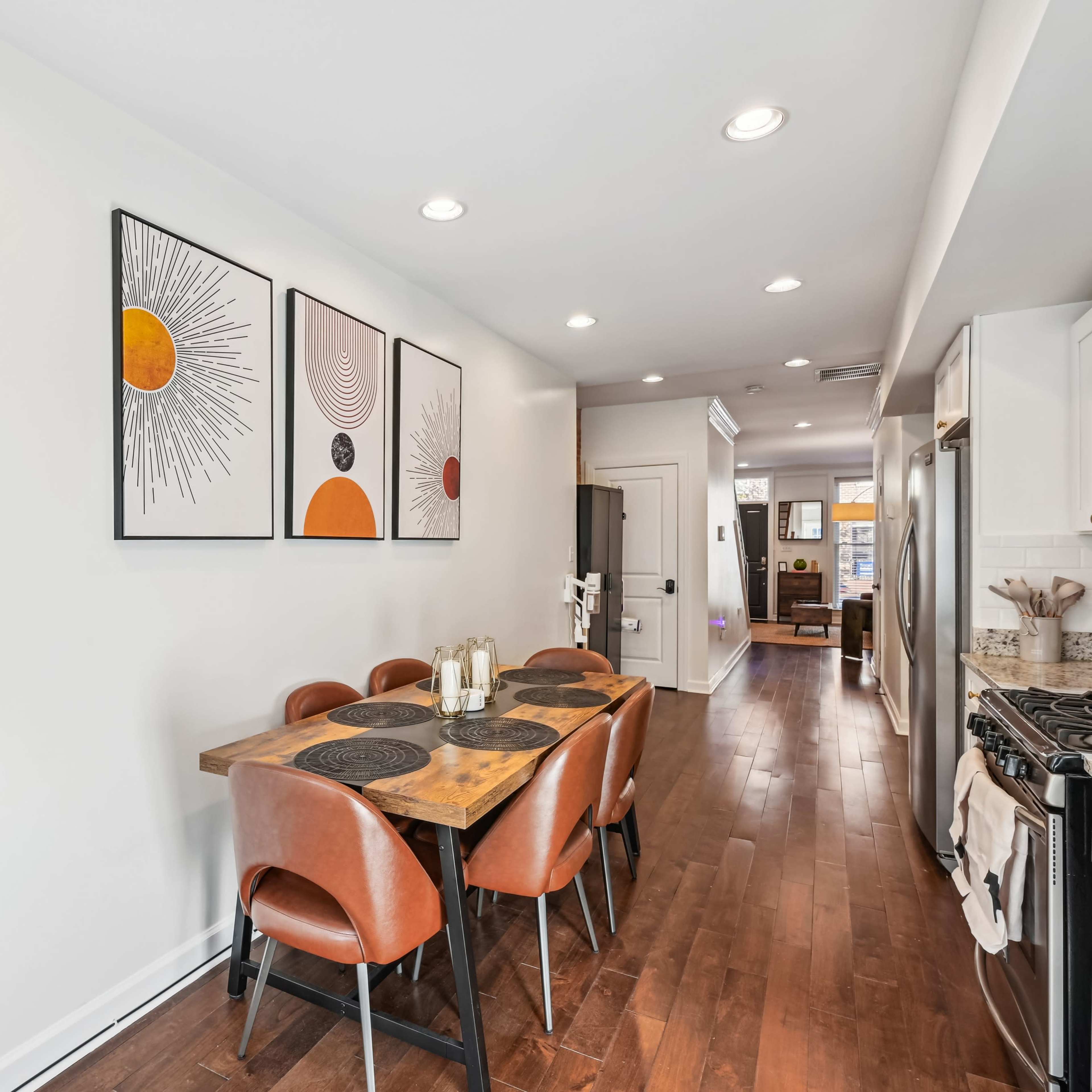 A modern dining area with a wooden table surrounded by brown chairs, and three framed abstract artworks on the wall.