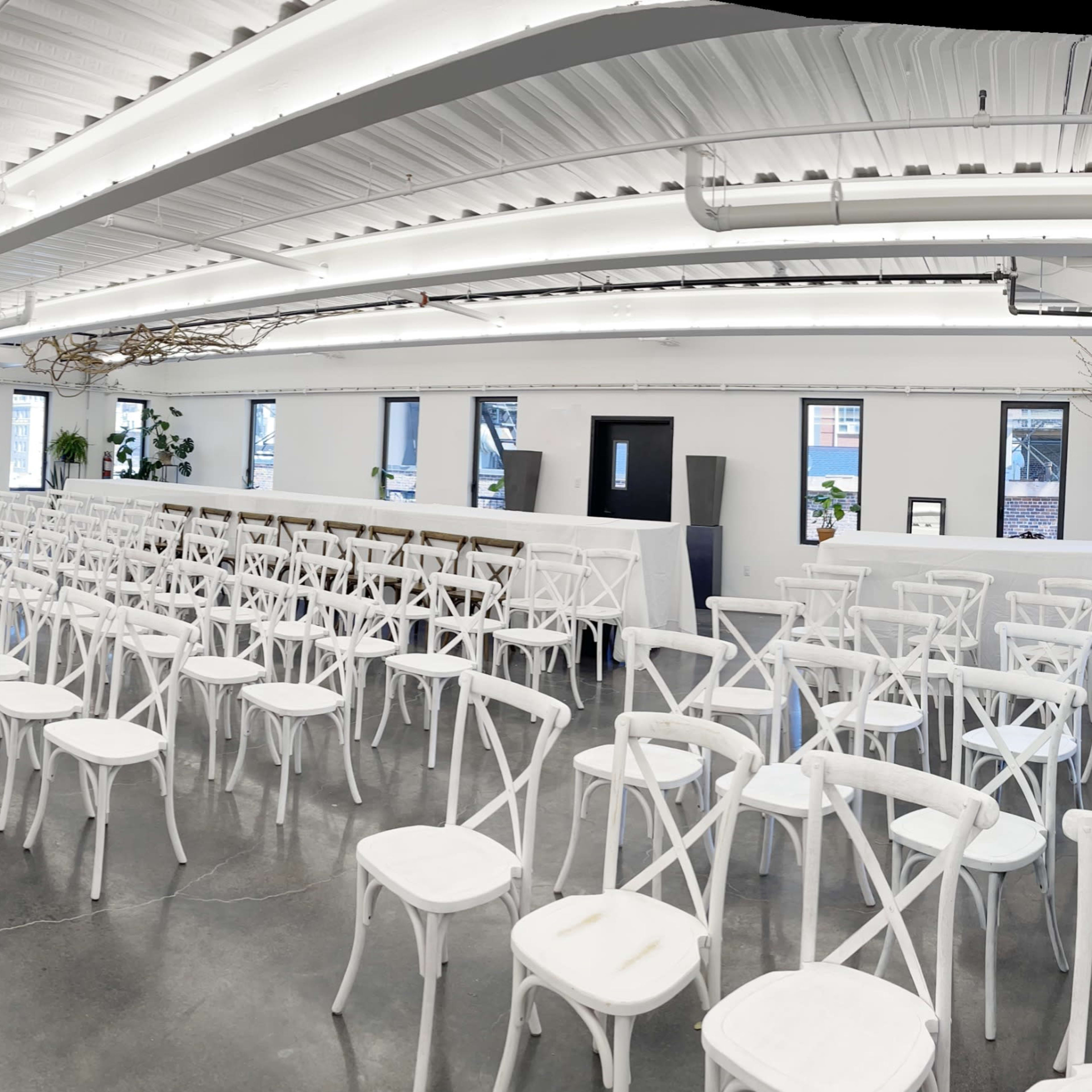 A spacious, well-lit event venue arranged with rows of white chairs facing a focal point at the front.