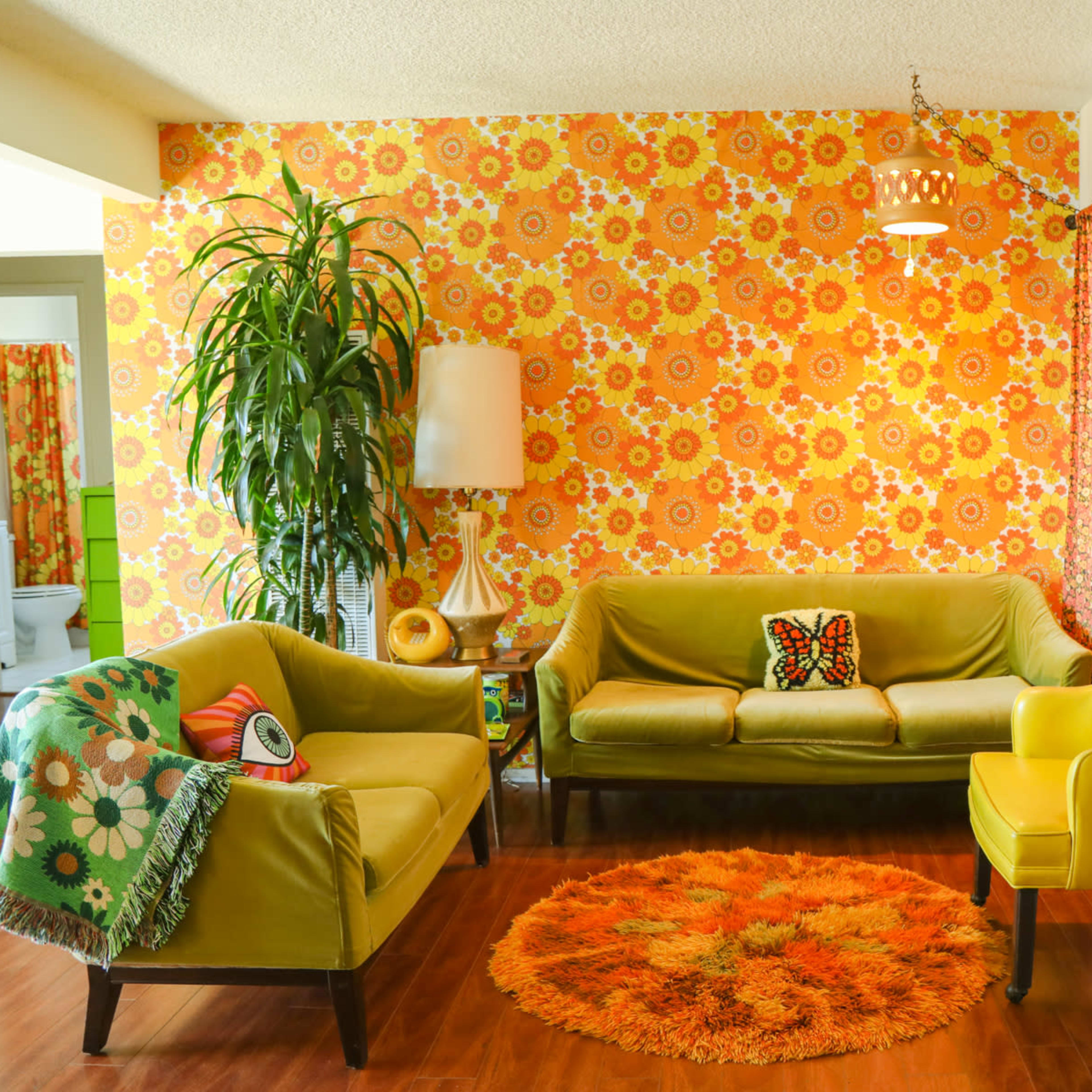 The living room features vibrant flower-patterned wallpaper, a green sofa, a yellow chair, and an orange circular rug.