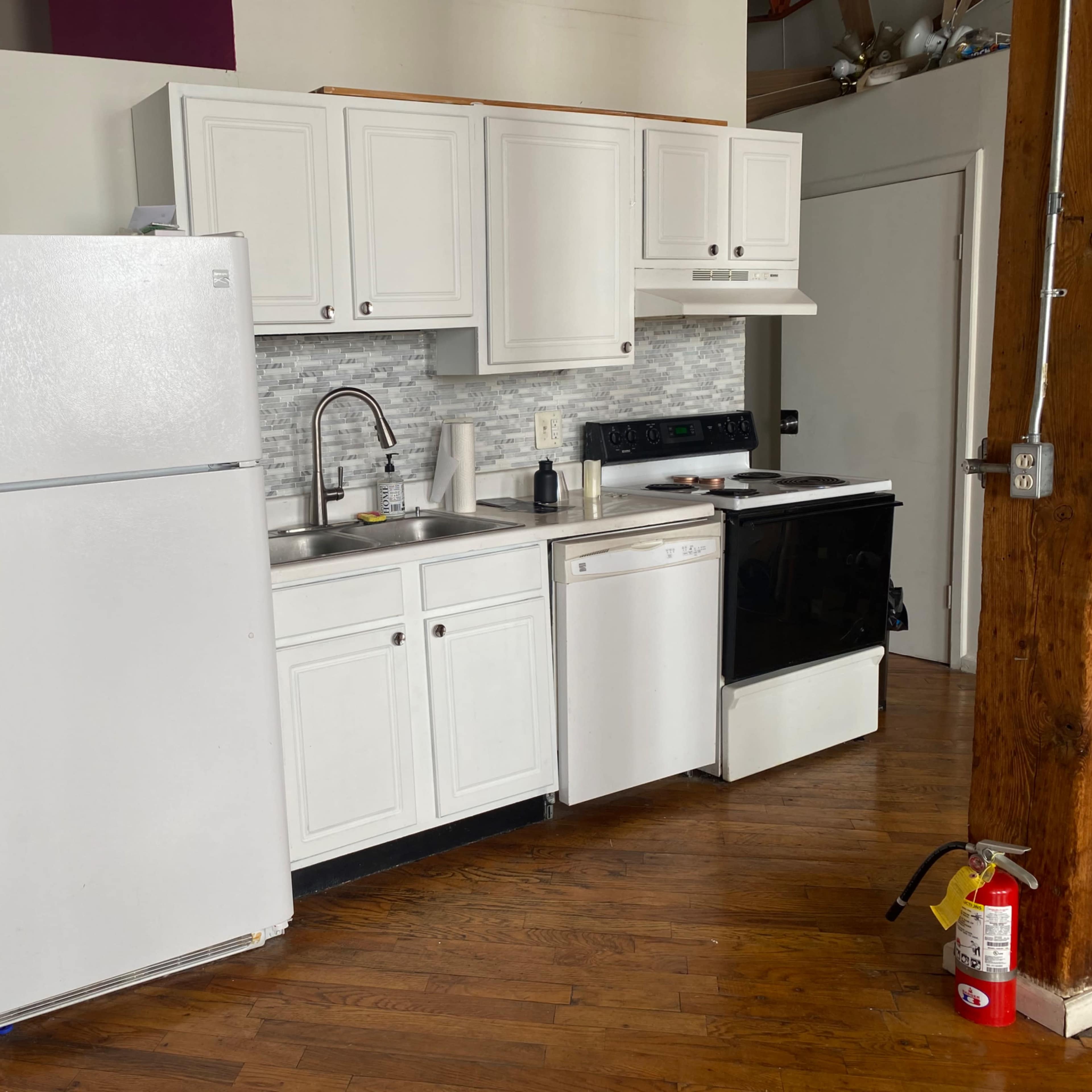 A kitchen with white cabinets, a stainless steel sink, and a refrigerator, dishwashers, and an oven arranged along a wooden floor.