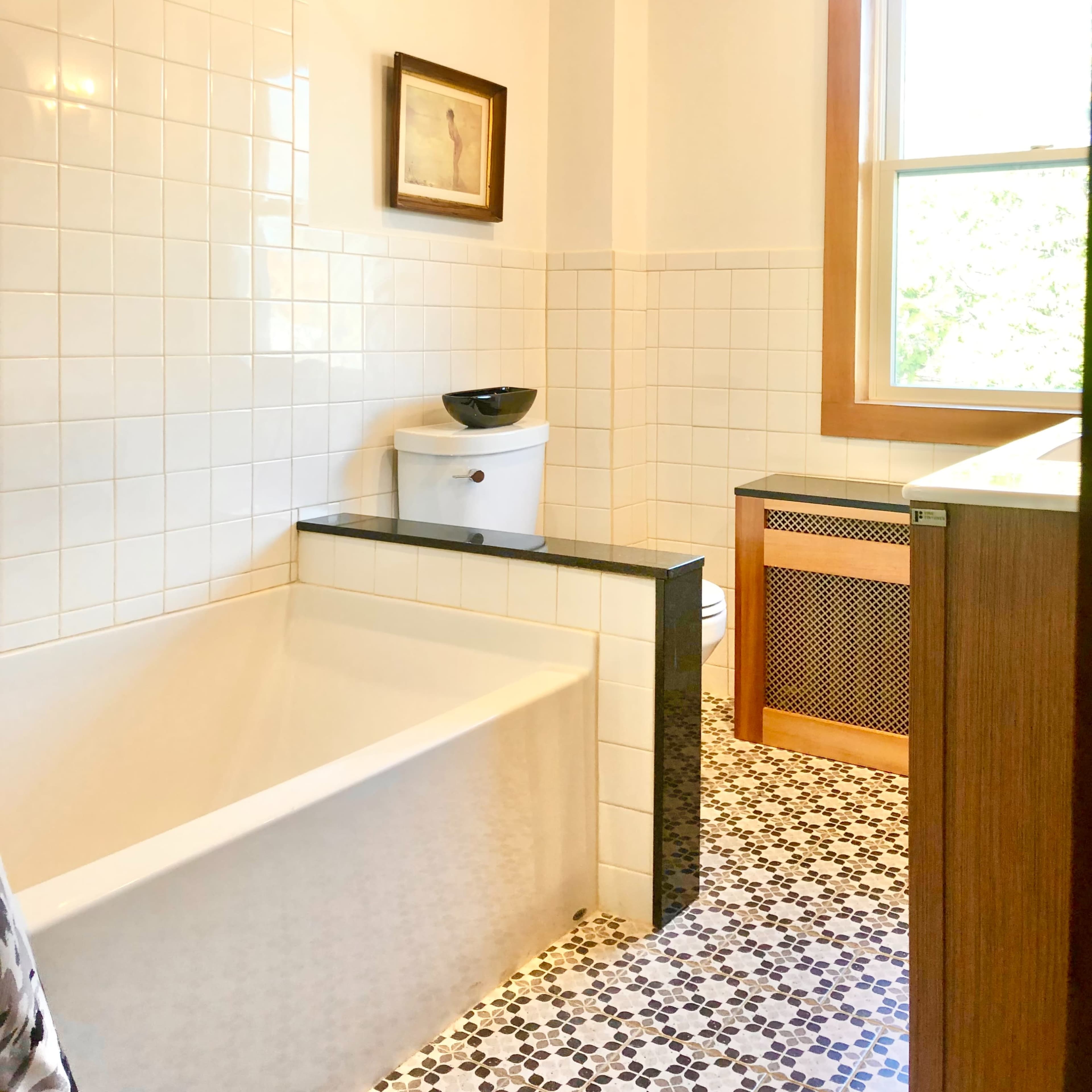 A modern bathroom featuring a bathtub, toilet, sink with cabinetry, and a window with natural light.