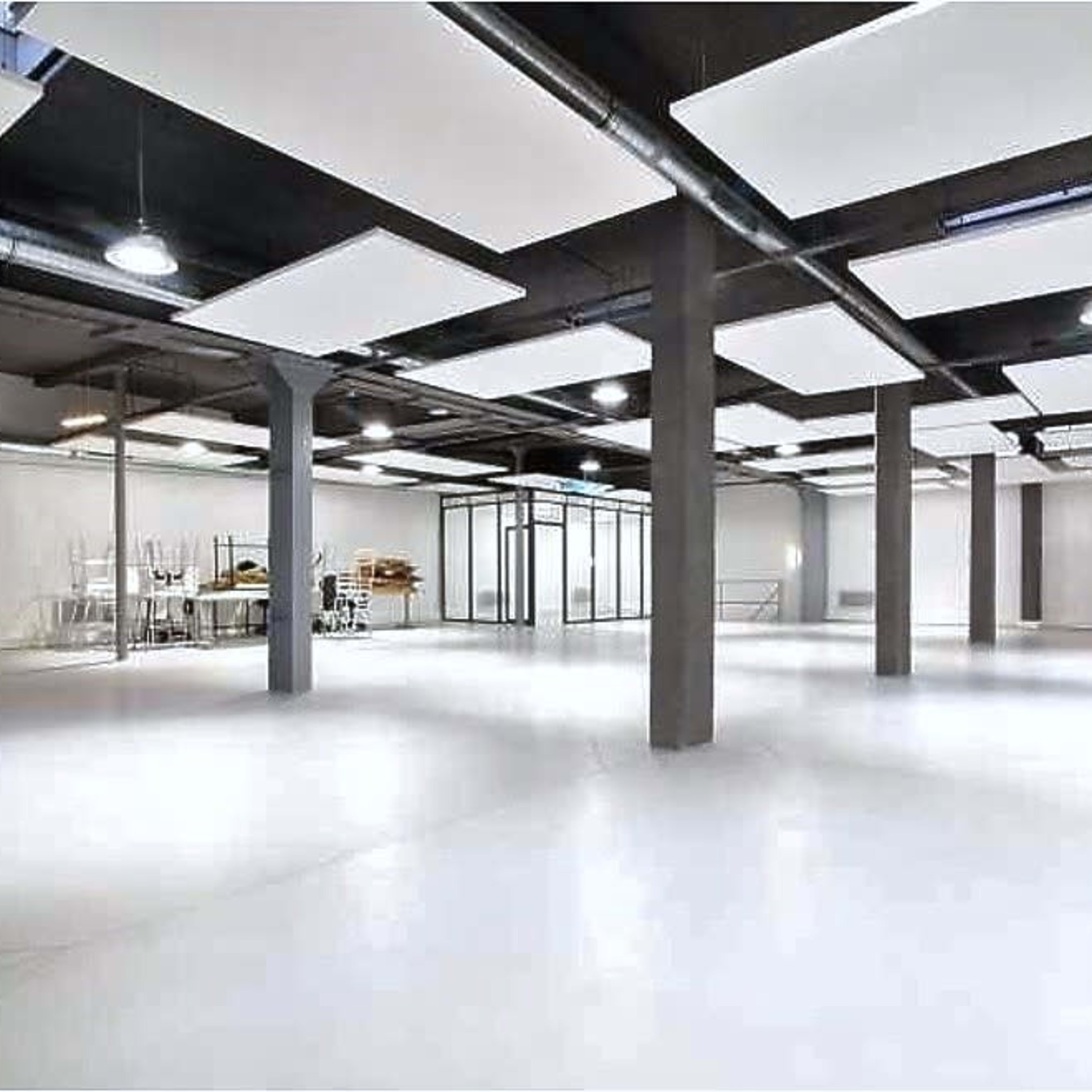 A spacious, empty room with white walls, a polished floor, and several hanging ceiling panels.