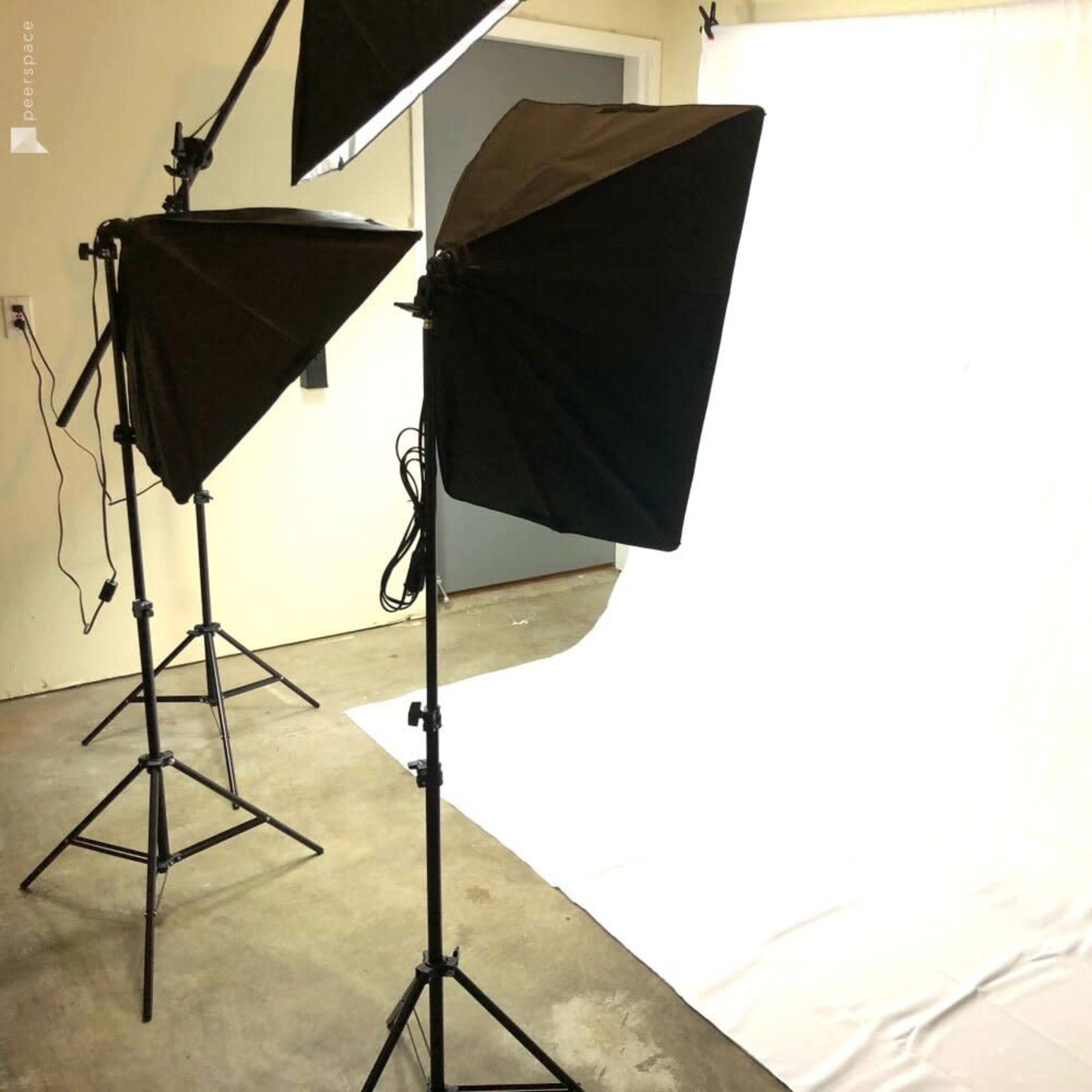 A photography studio setup with three softbox lights directed towards a plain white backdrop.