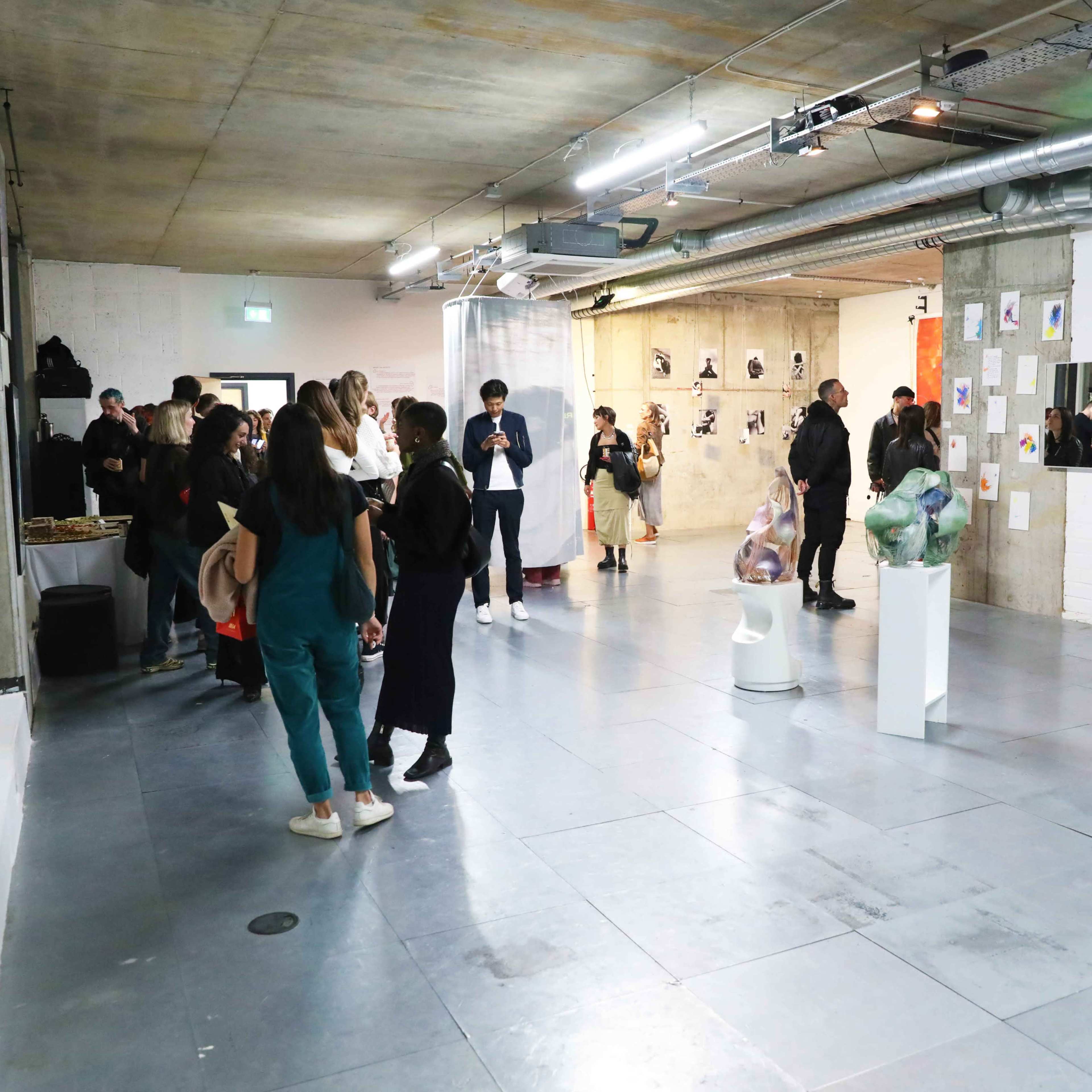 A contemporary art gallery filled with people engaging with various artworks displayed on the walls and in the center of the room.