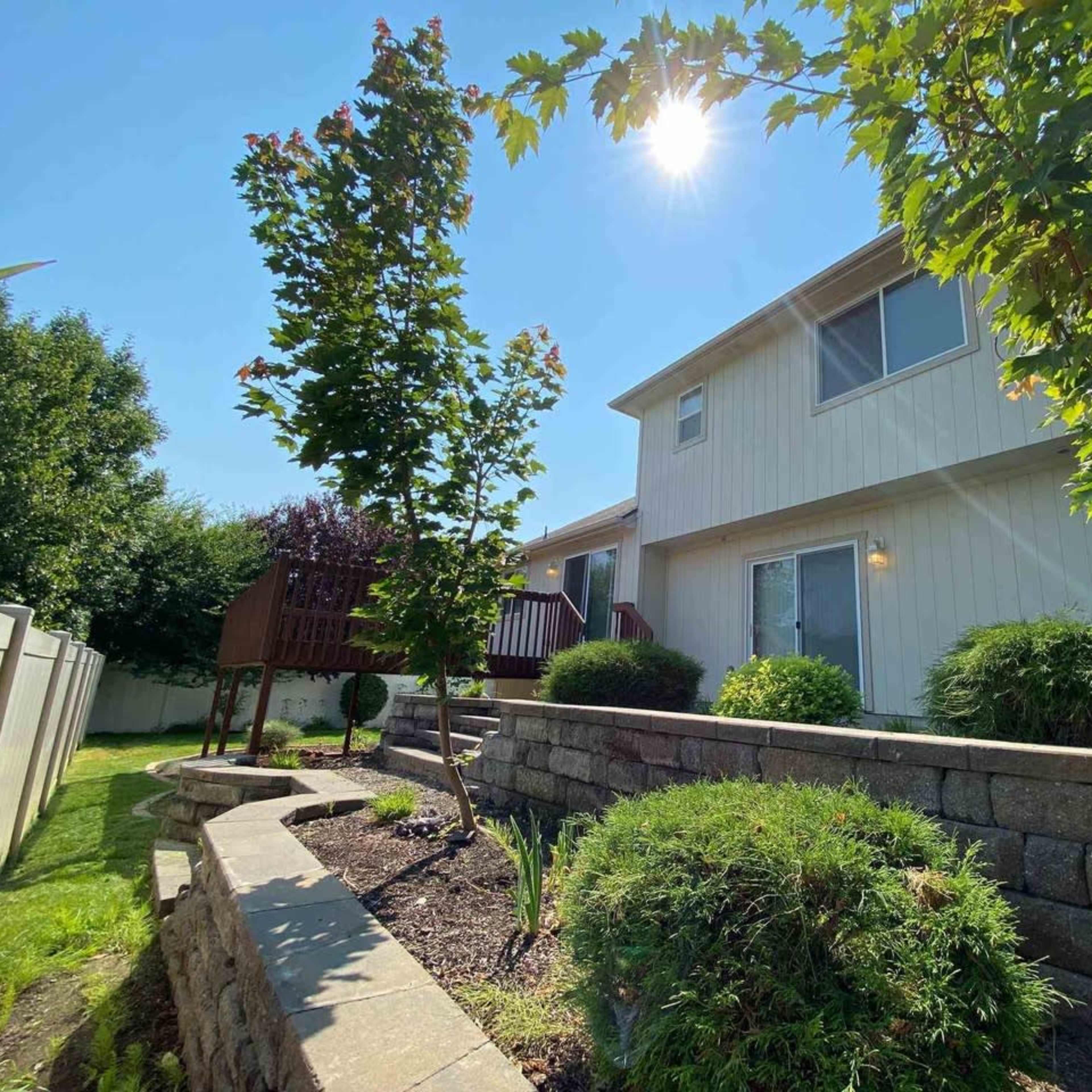 A two-story house with a landscaped yard and a wooden play structure is shown under a bright sun.