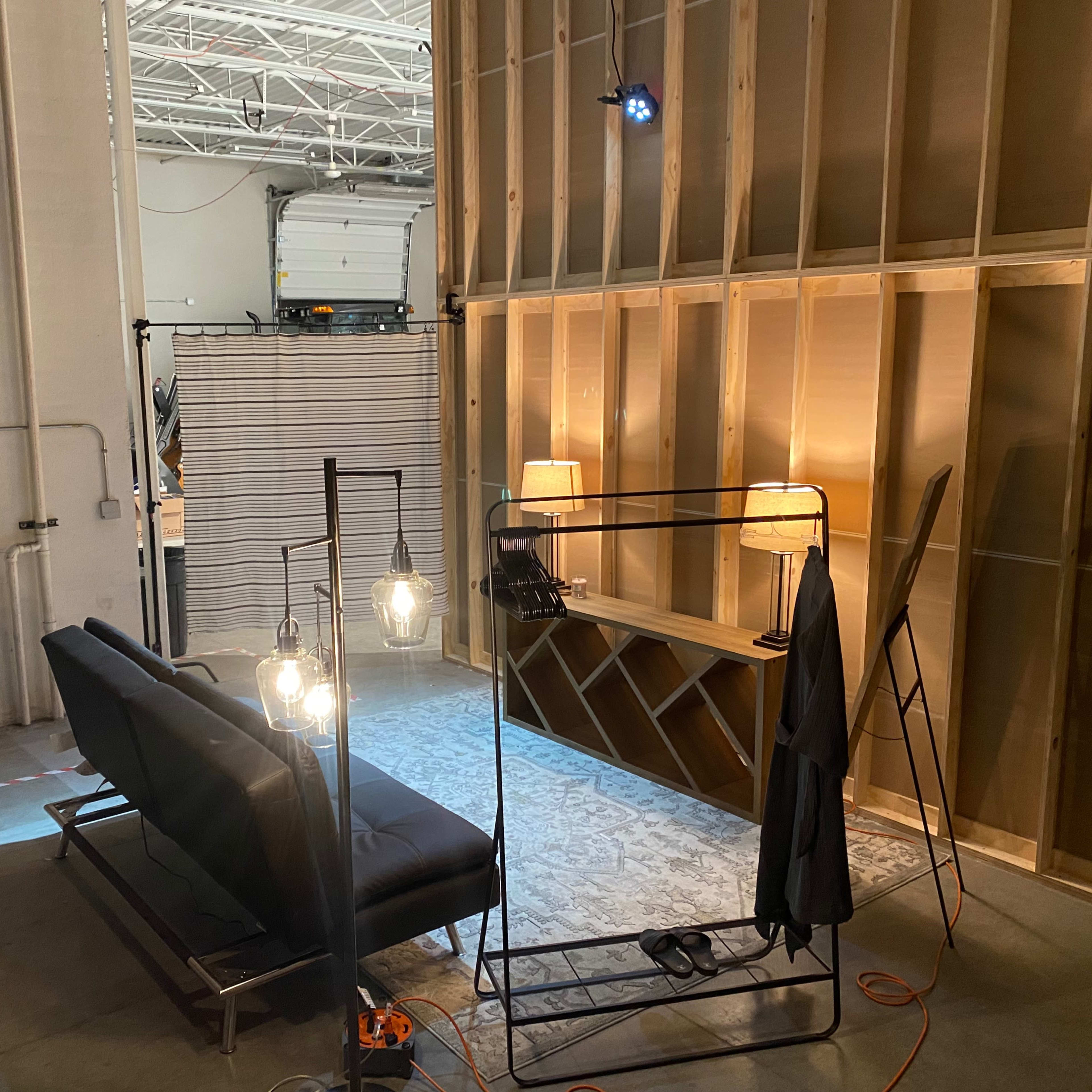 A sparsely furnished interior space with a sofa, lamps, and a backdrop of wooden walls under construction.