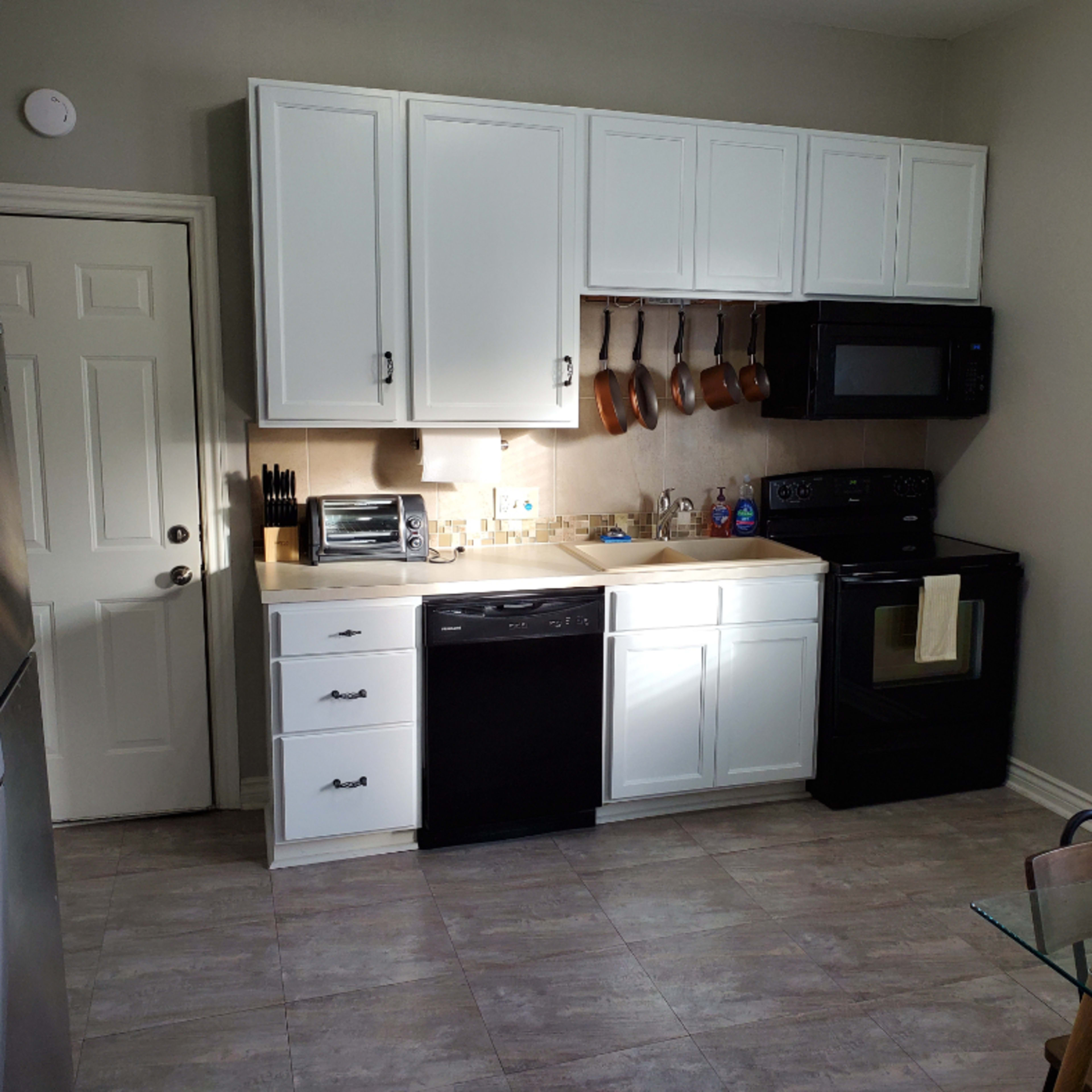 The kitchen features white cabinets, a black stove and microwave, and stainless steel appliances.