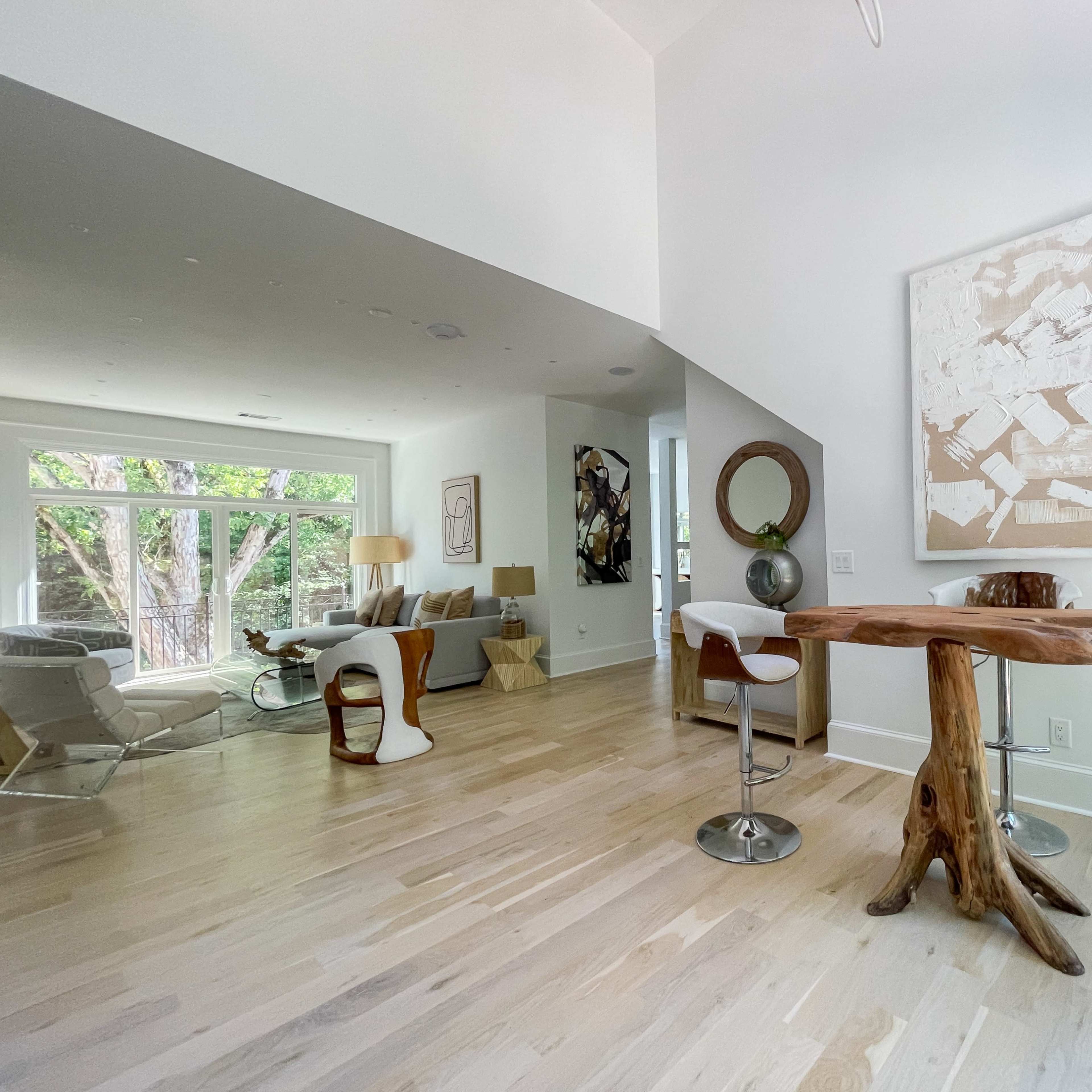 The scene shows a modern interior space featuring a seating area with large windows, a small wooden table, and contemporary chairs.
