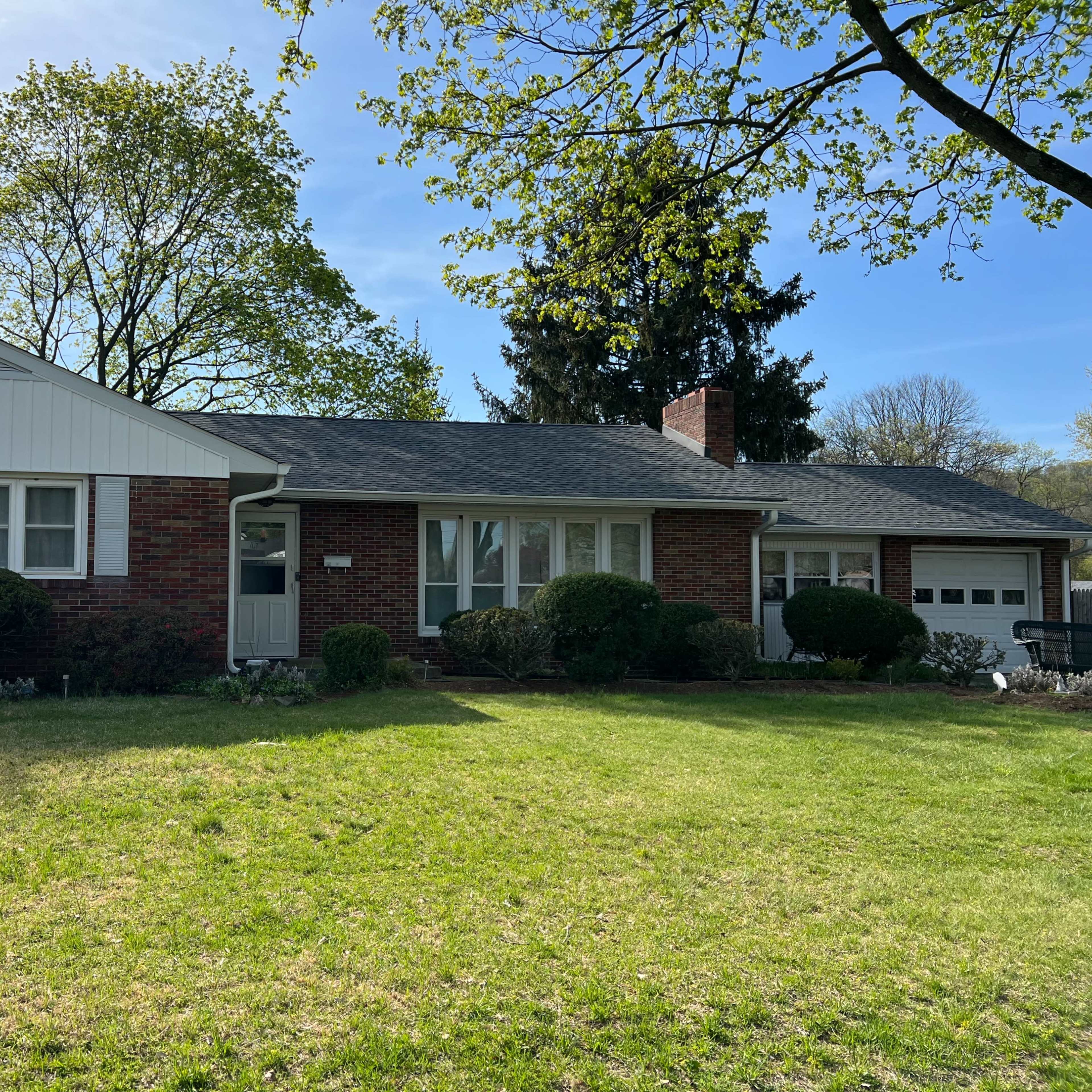 A single-story brick house with a front lawn, trees, and a driveway.