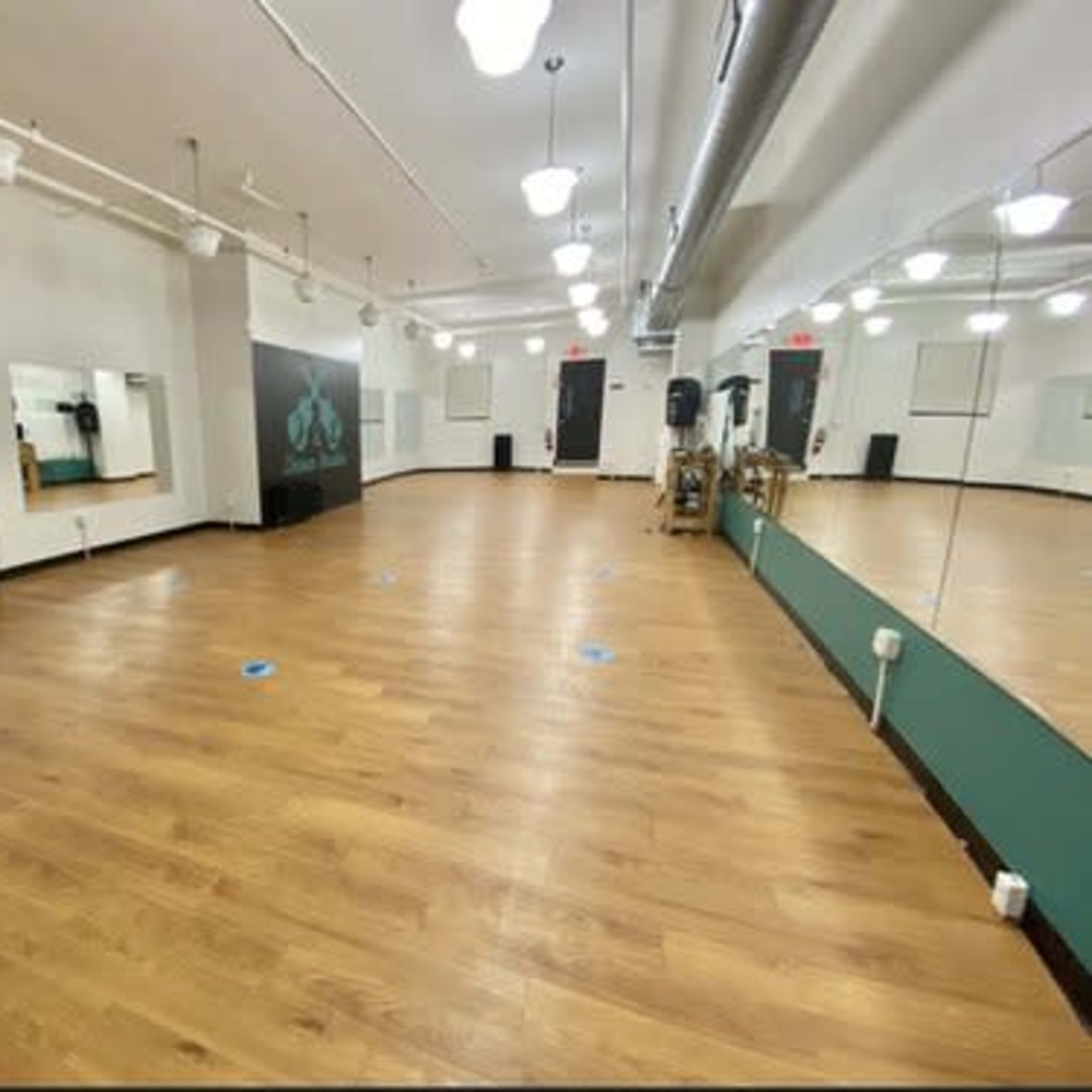 A spacious, empty dance studio with wooden flooring and mirrors on two walls.