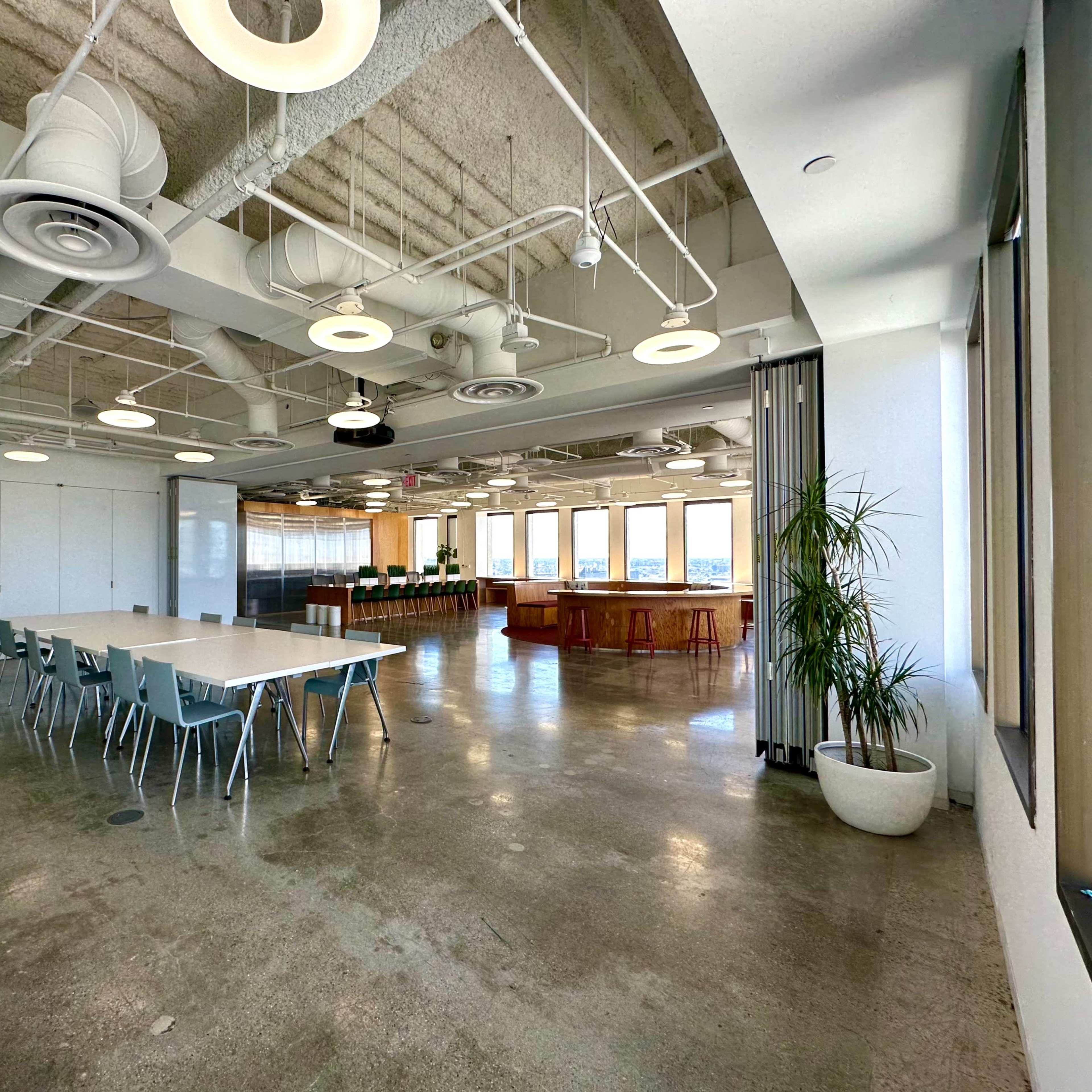 A large, modern conference room features a long table with chairs, a presentation area, and windows offering city views.