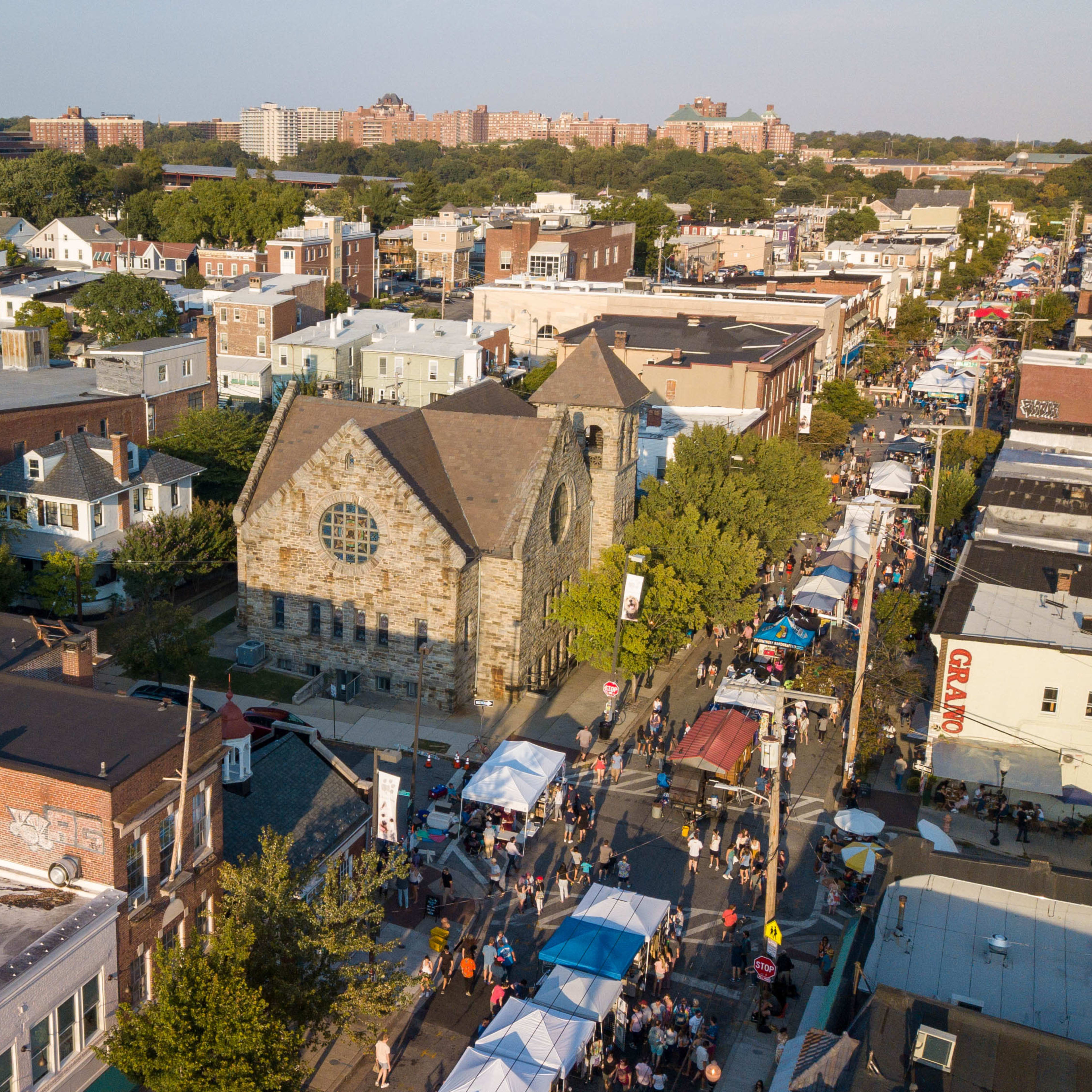 An aerial view of a busy street market with stalls and crowds near a historic stone church surrounded by residential buildings.