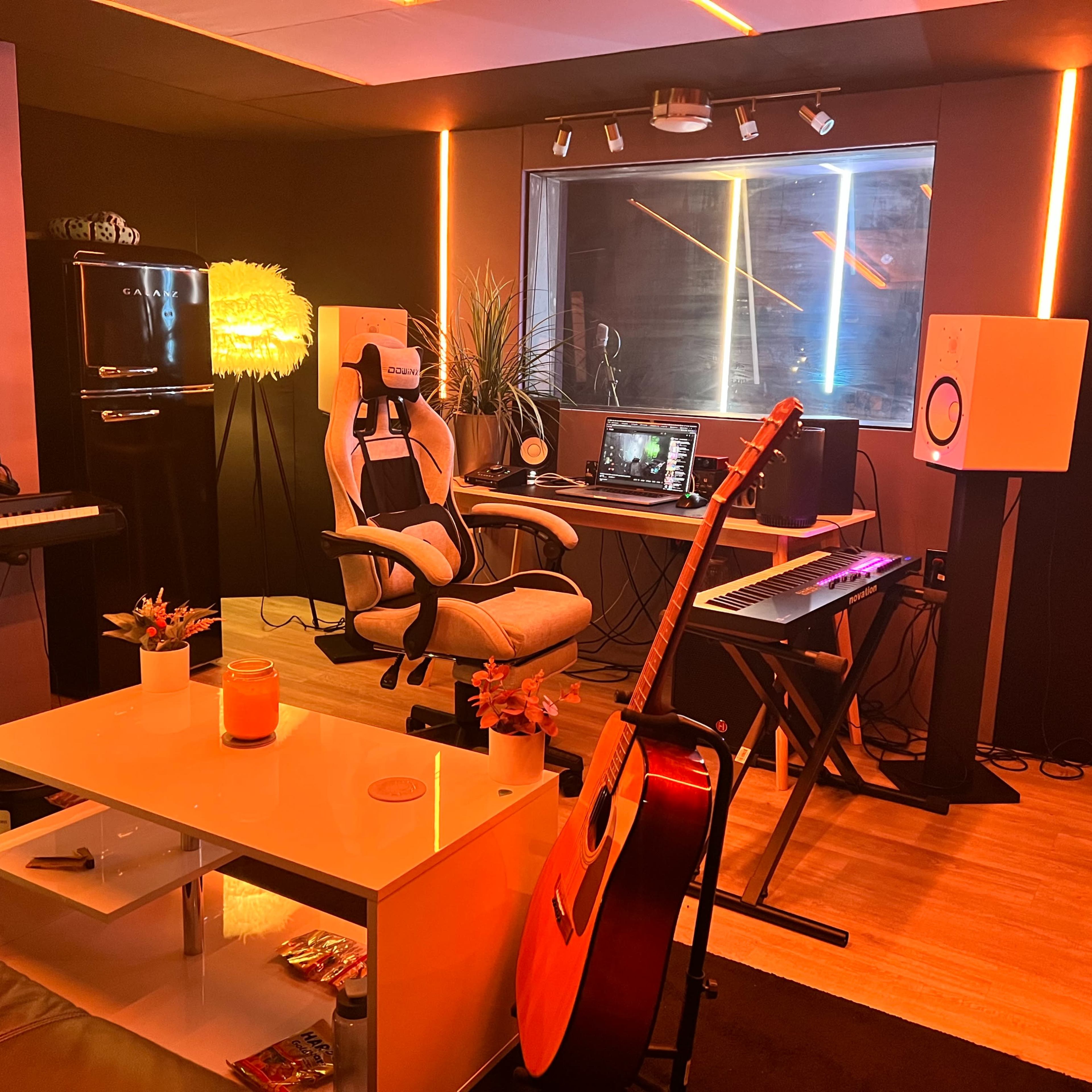 A modern music studio with a desk, computer, musical instruments, and ambient lighting.