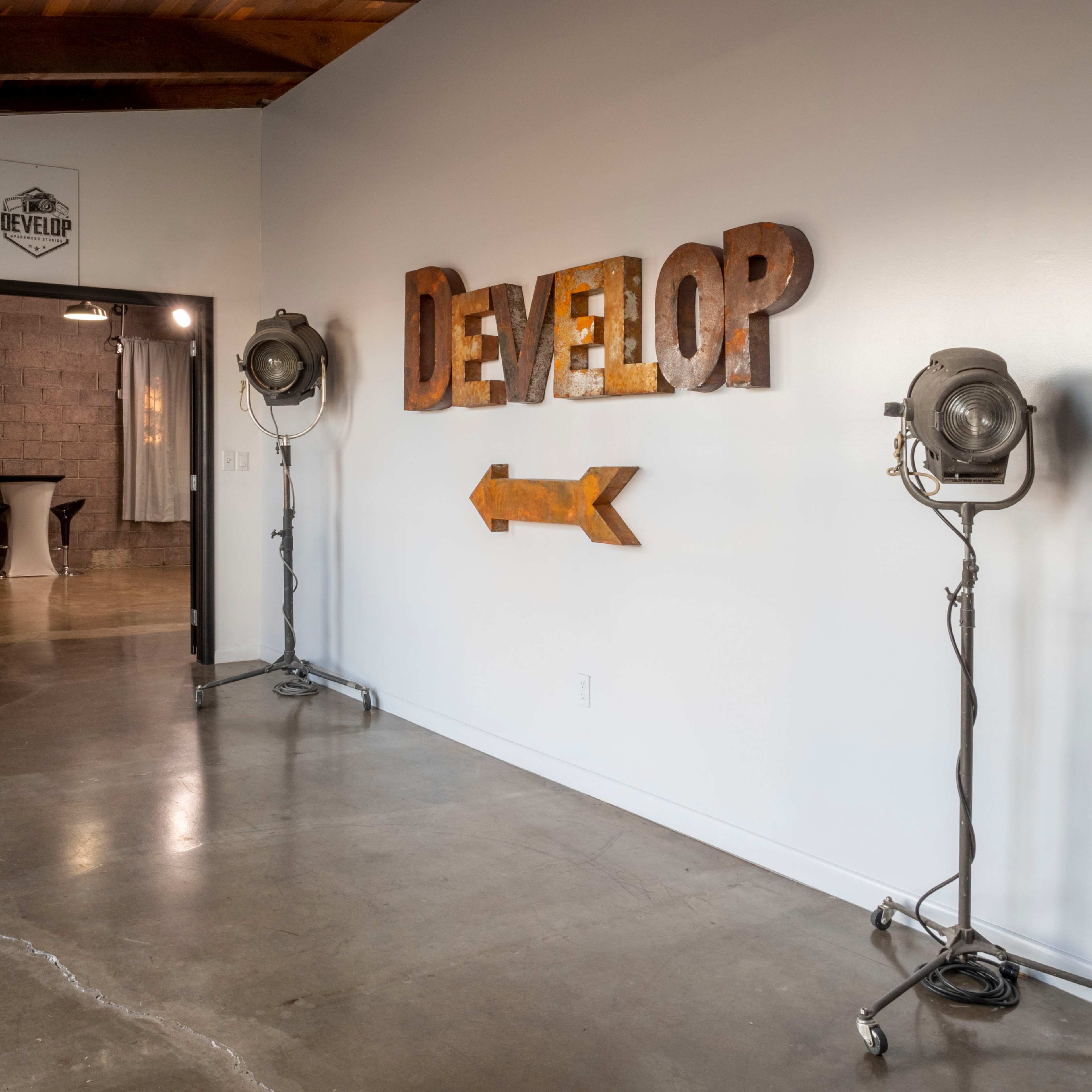 A stylish interior space featuring a large "DEVELOP" sign on the wall, two studio lights on either side, and a doorway leading to another room in the background.