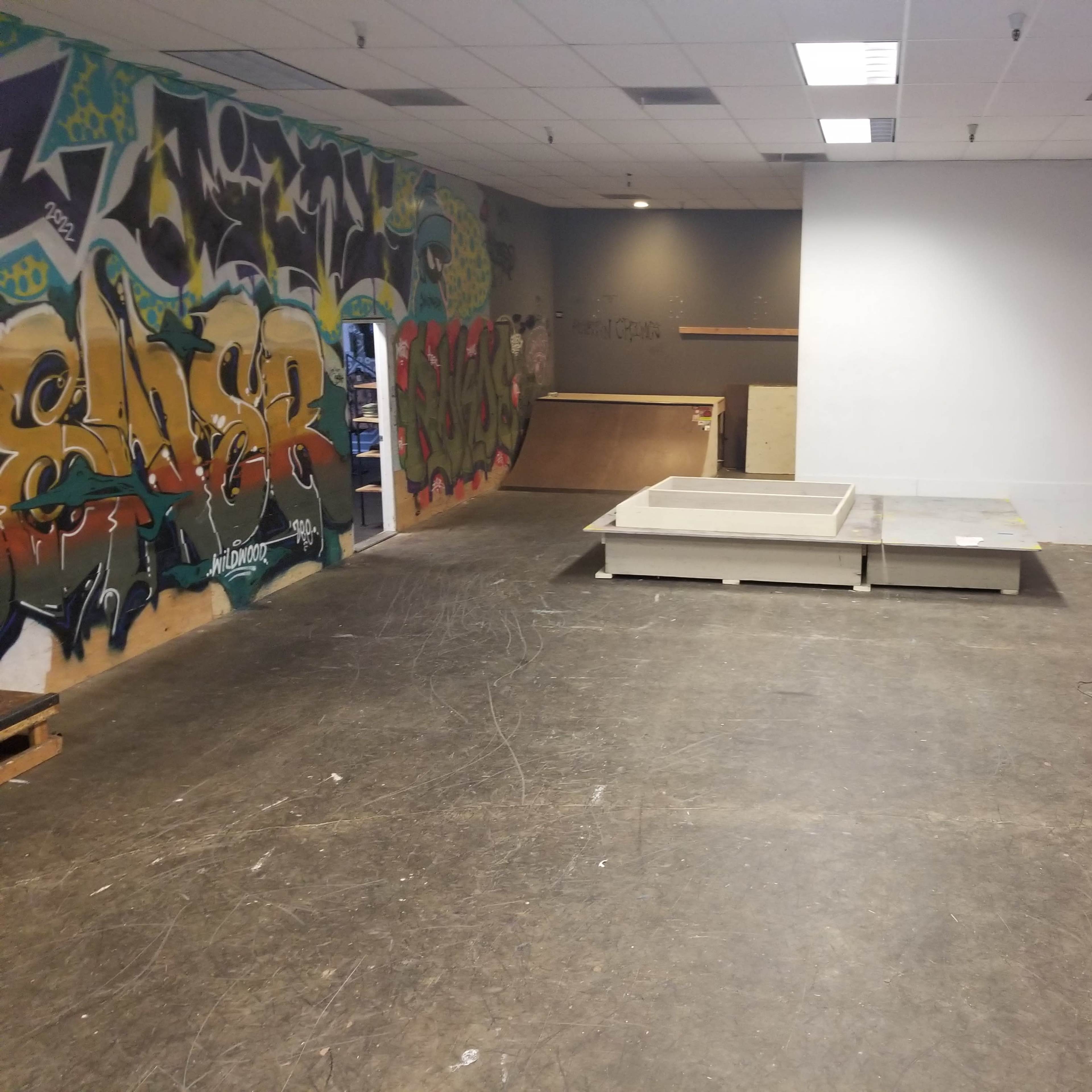 An indoor skate park with graffiti-covered walls, a rectangular wooden ramp, and some skateboarding equipment.