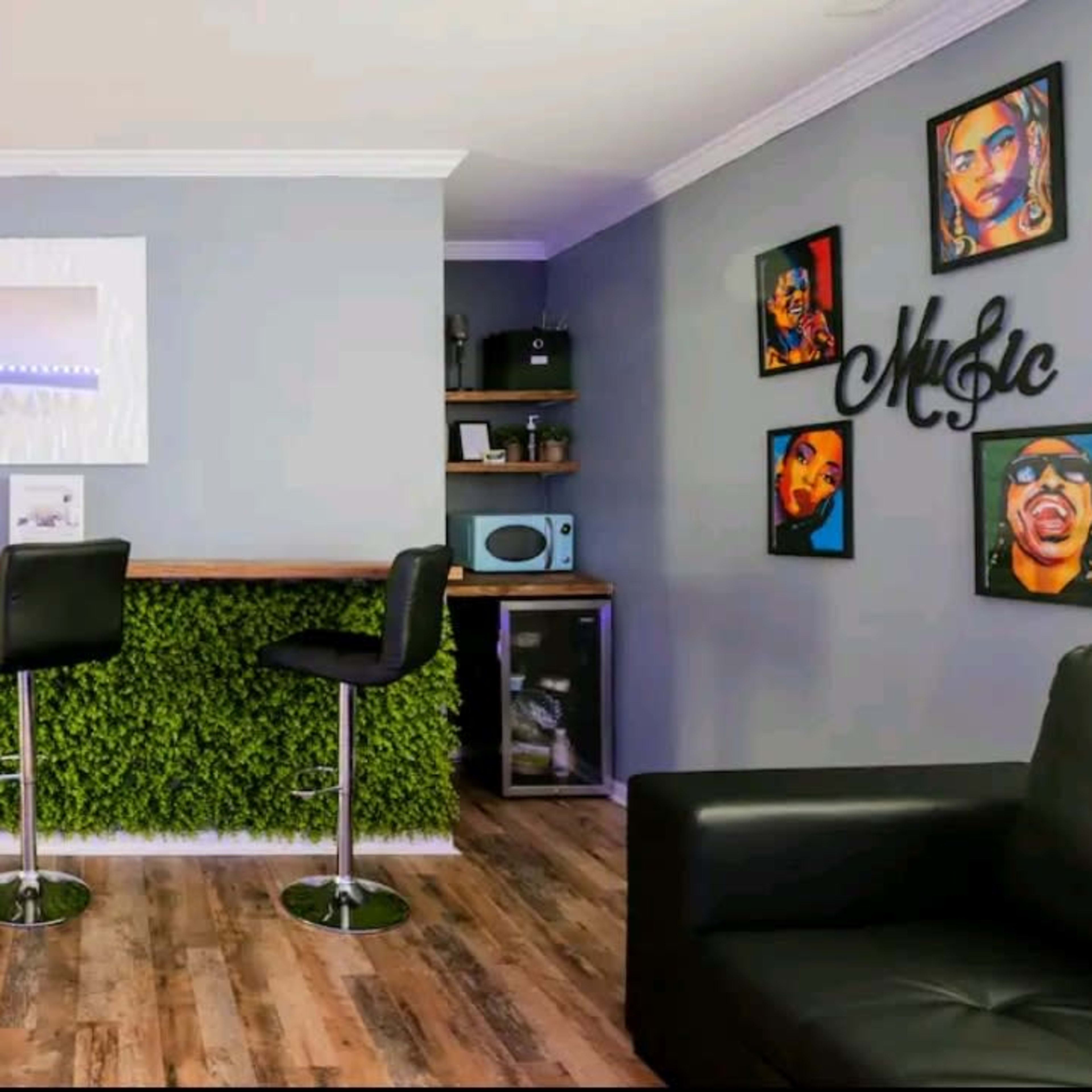 A modern interior with a bar area featuring four black stools, a wall covered in greenery, and framed portraits of musicians.