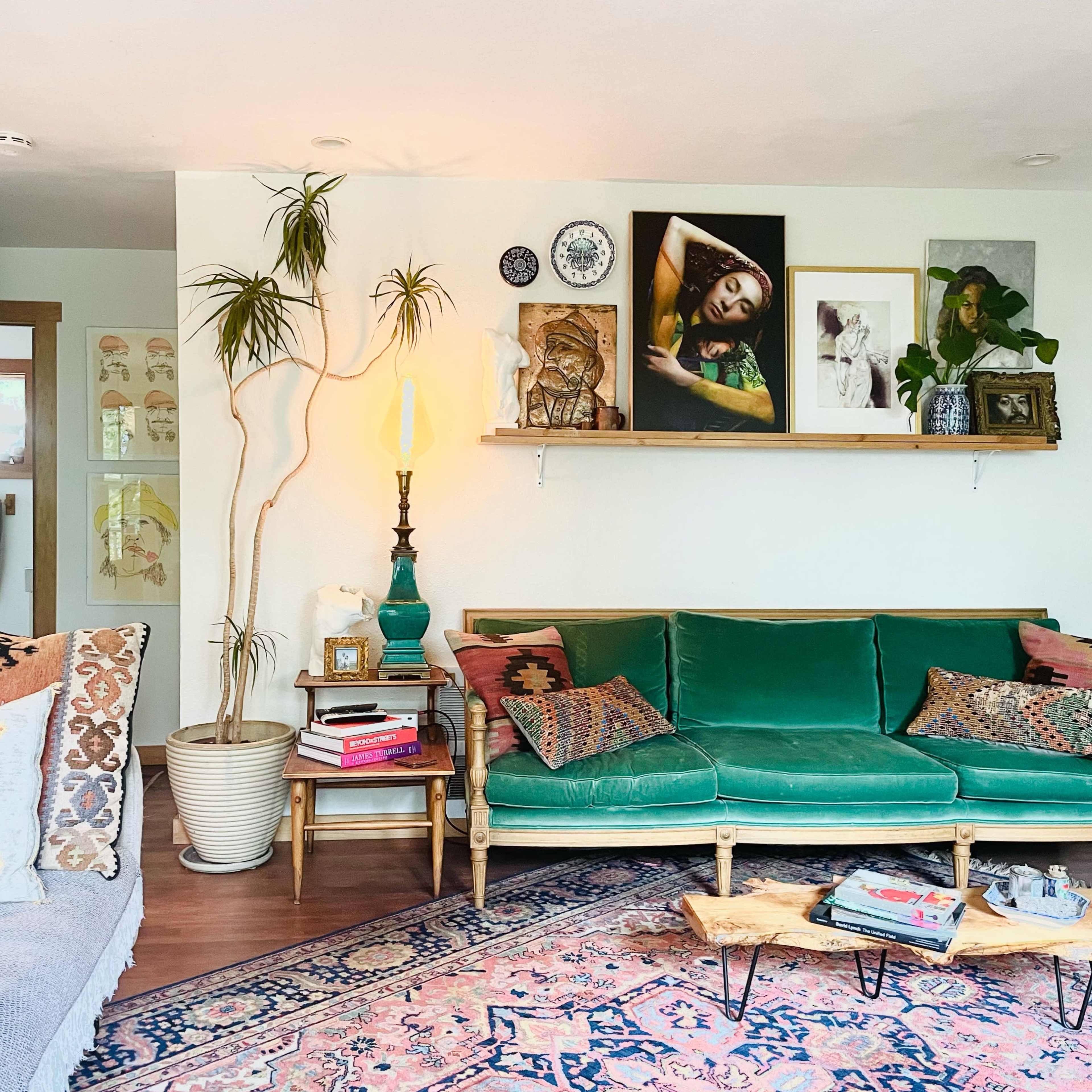 The living room features a green sofa with decorative pillows, a wooden coffee table, and a shelf displaying various artworks and plants.