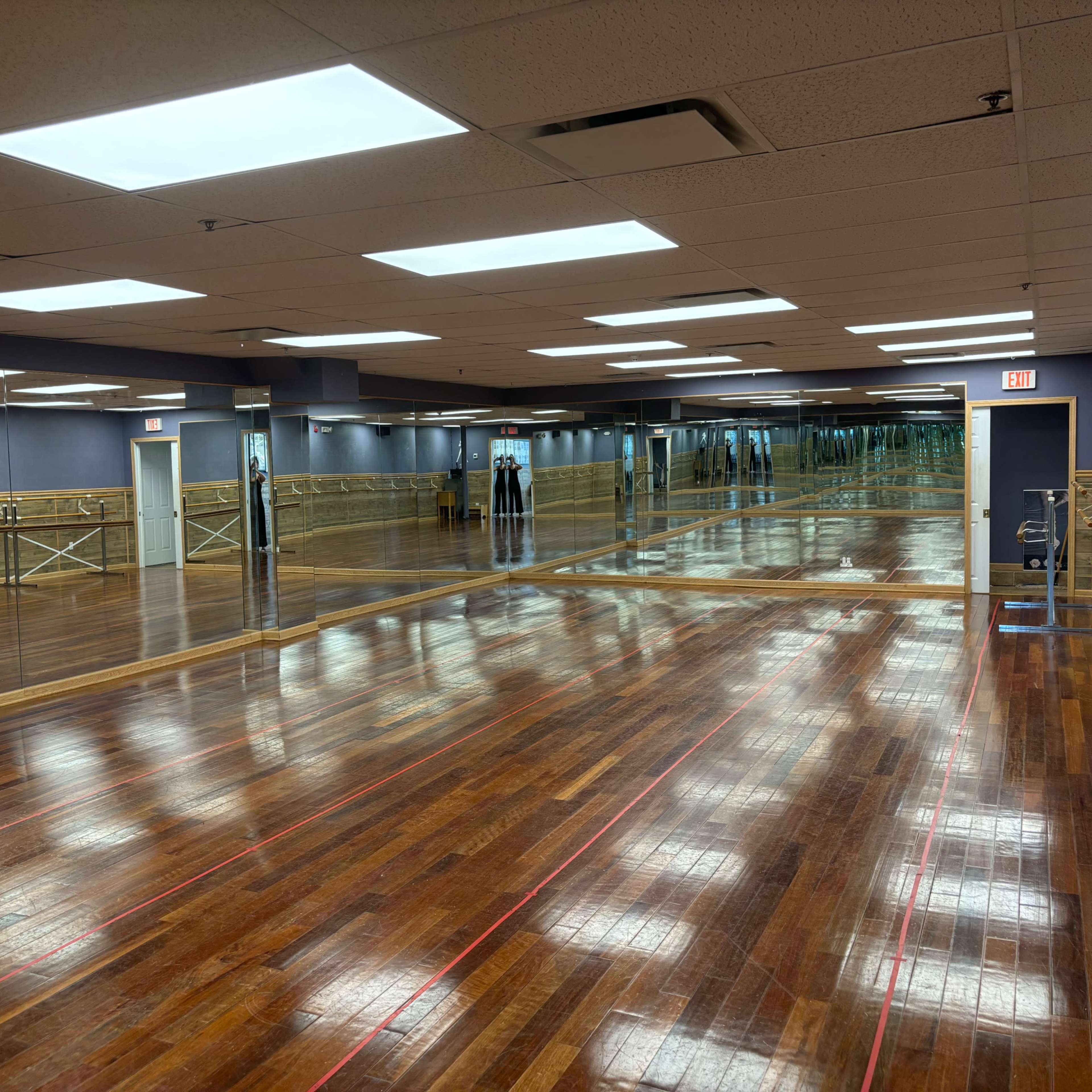 A spacious dance studio with wooden floors, mirrored walls, and bright overhead lighting.