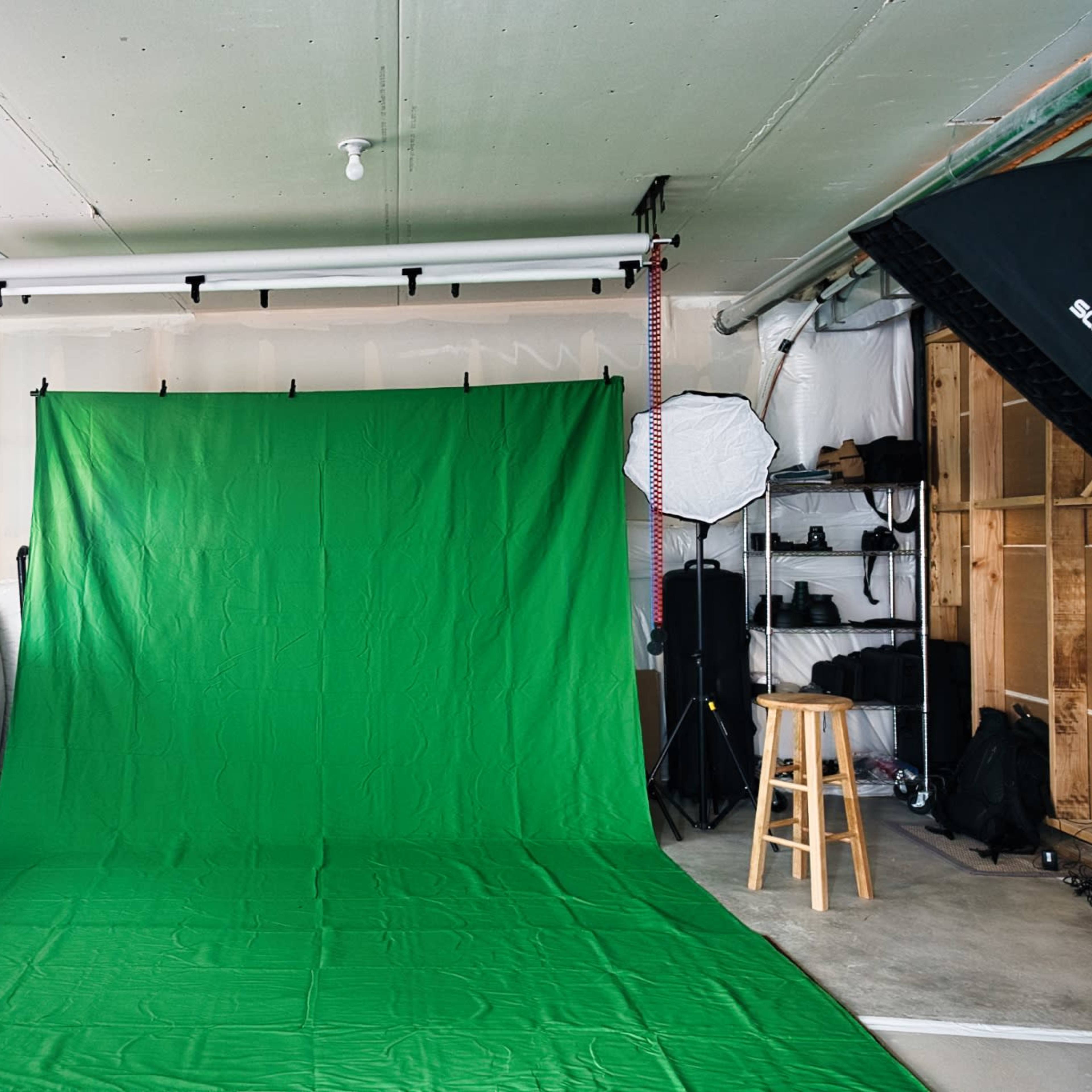 A green backdrop is set up in a well-lit studio space with various lighting equipment and a stool.