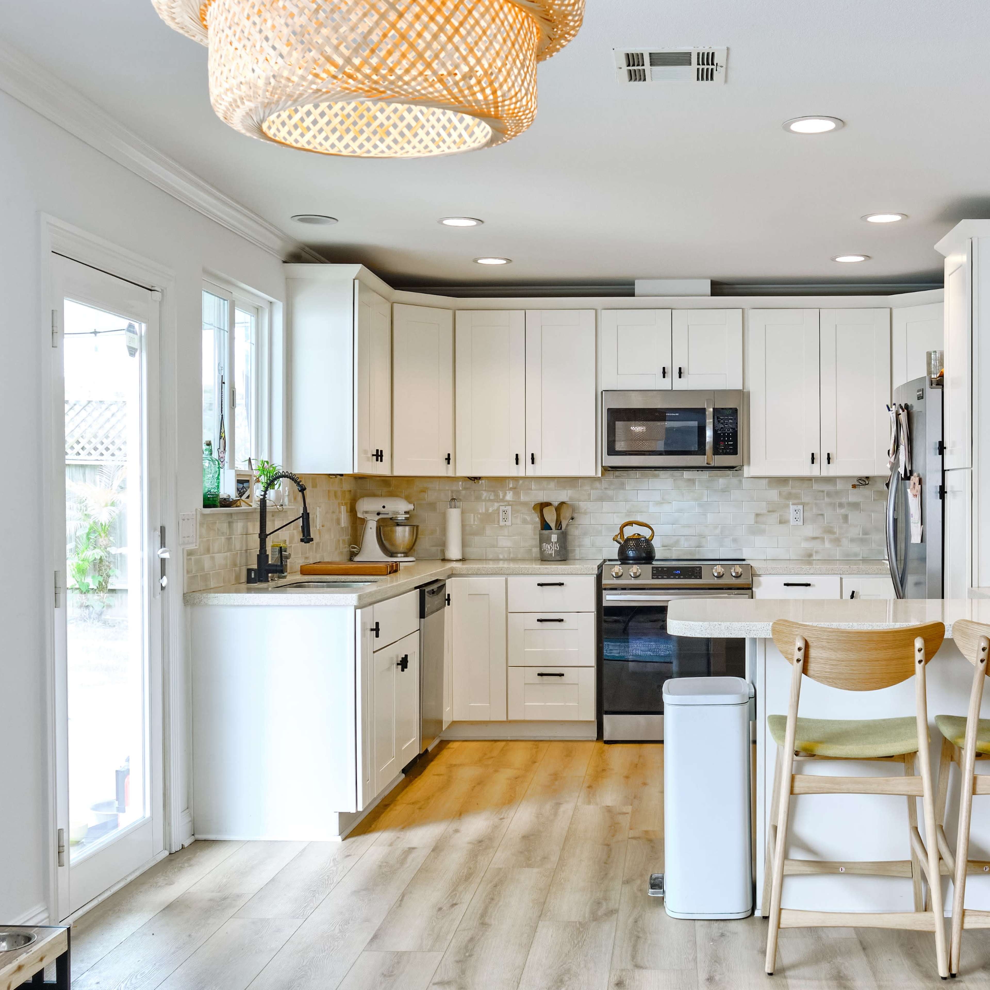 A modern kitchen with white cabinetry, stainless steel appliances, and a breakfast bar with three wooden stools.