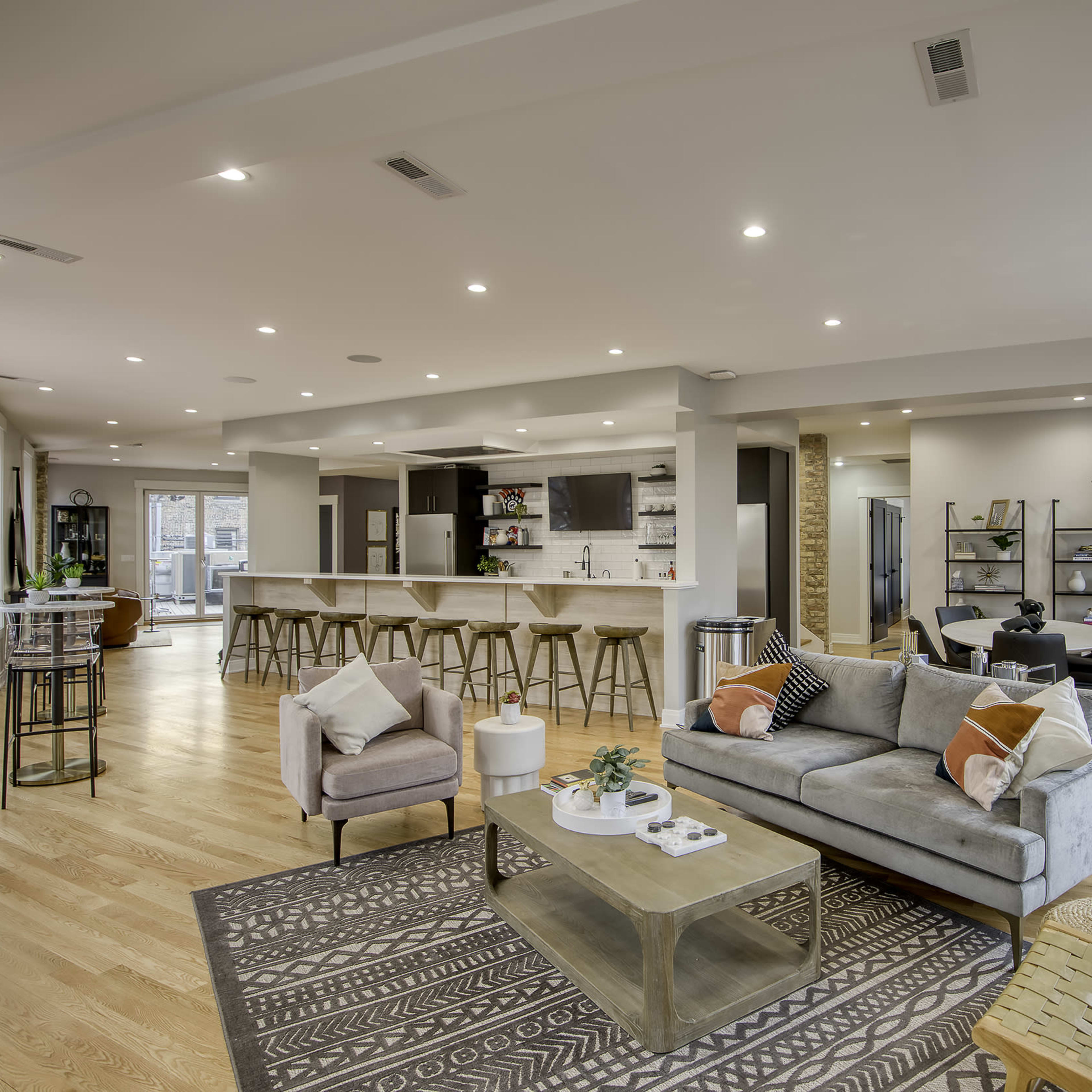 A spacious modern living area with a gray sofa, a glass coffee table, a dining area, and large windows allowing natural light to fill the space.
